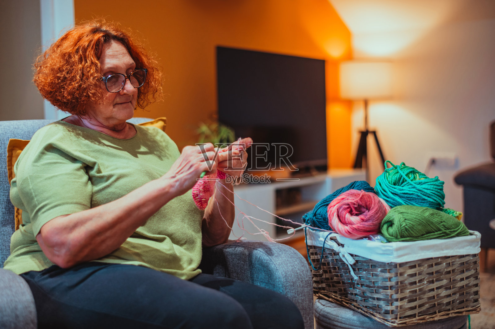 成熟的女人坐在家里的扶手椅上编织。照片摄影图片