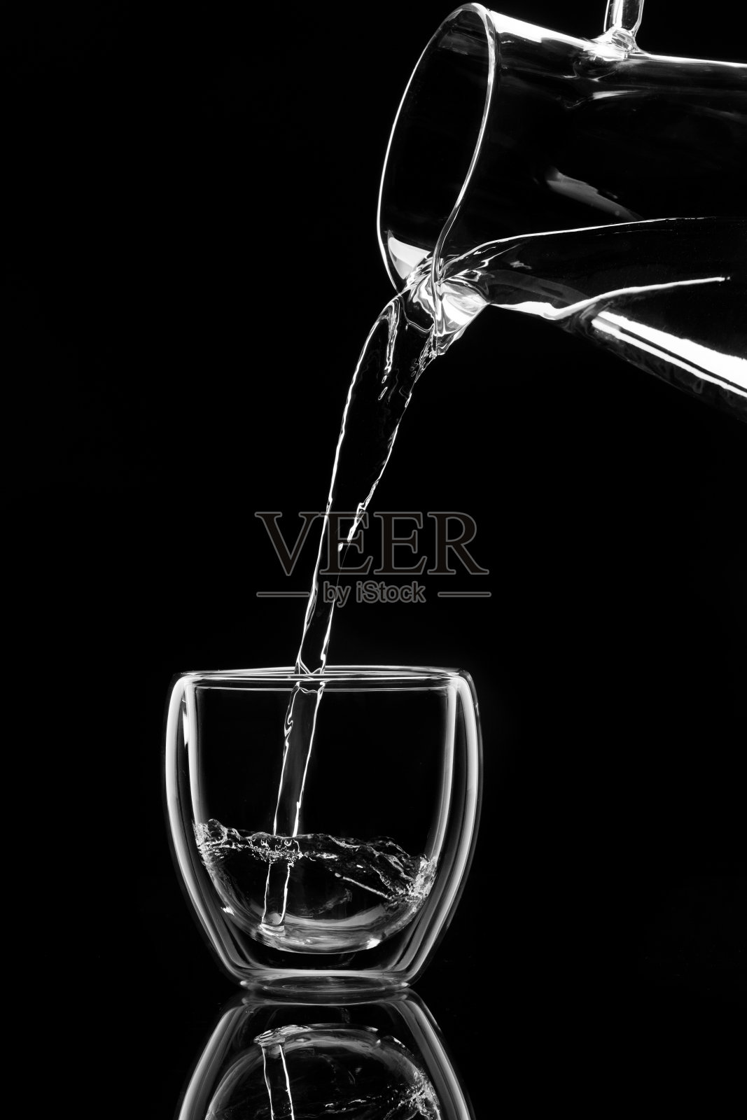 水在黑色的背景下从玻璃瓶中倒入玻璃杯照片摄影图片