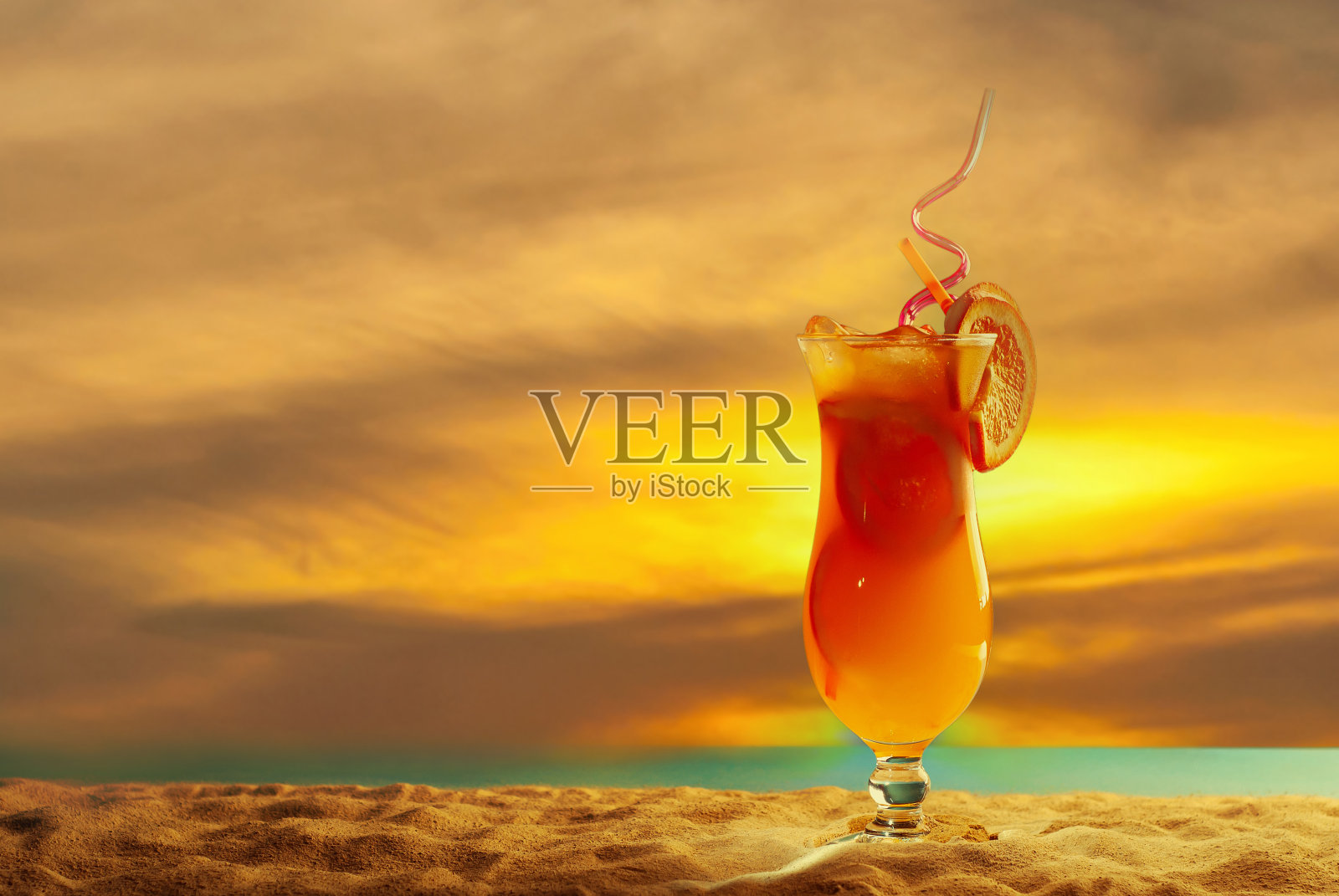 沙滩上的橙色鸡尾酒。酒精饮料加冰，橙沙上合。落日，大海和天空的背景。复制空间和玻璃附近的文本空闲空间。照片摄影图片