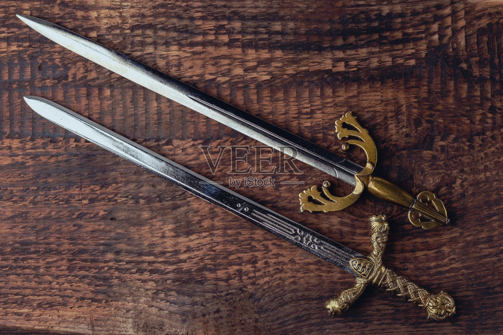 两把古色古香的骑士剑，背景是灰色的木纹。照片摄影图片