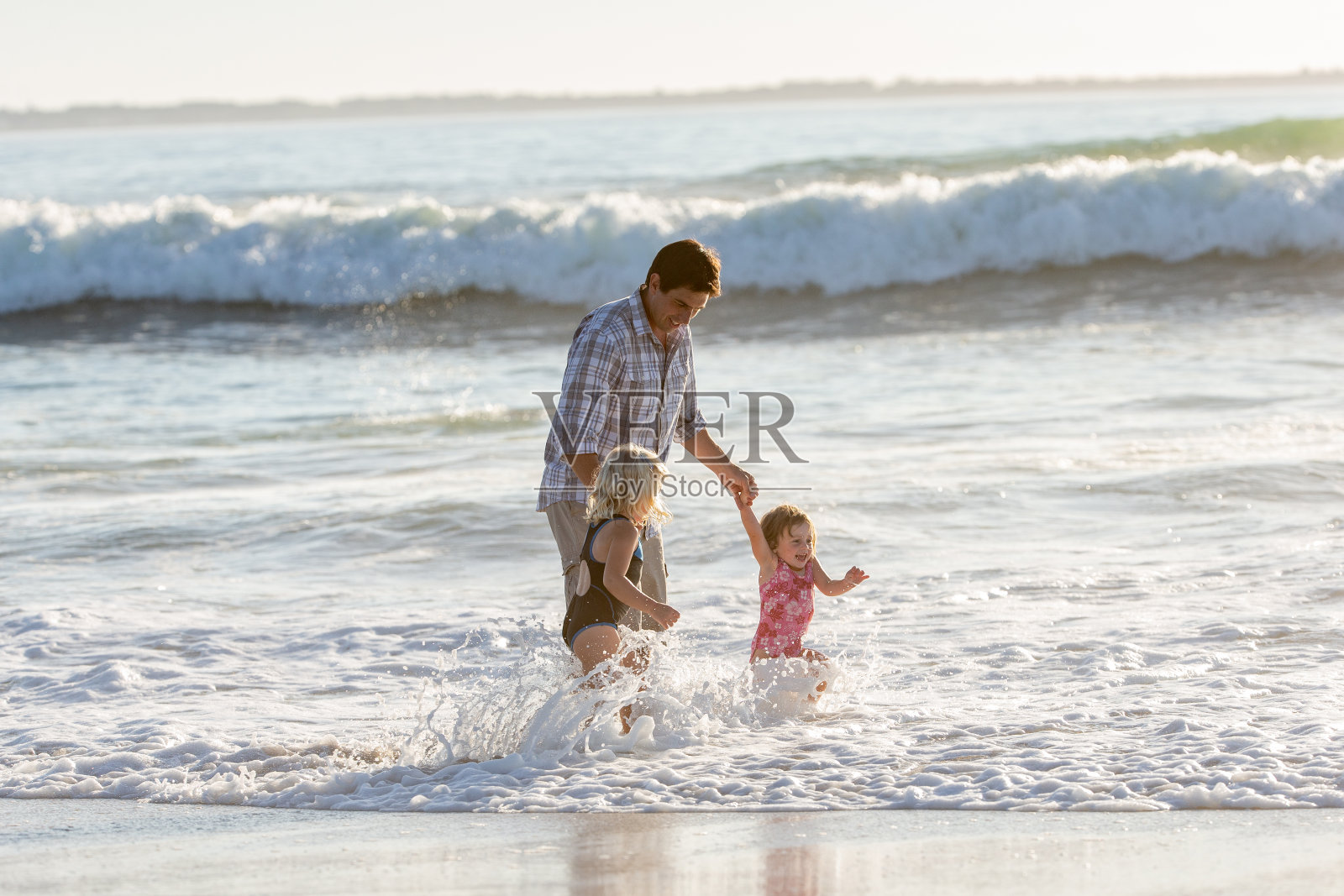 父亲和他的两个小女儿在海滩上玩海浪照片摄影图片