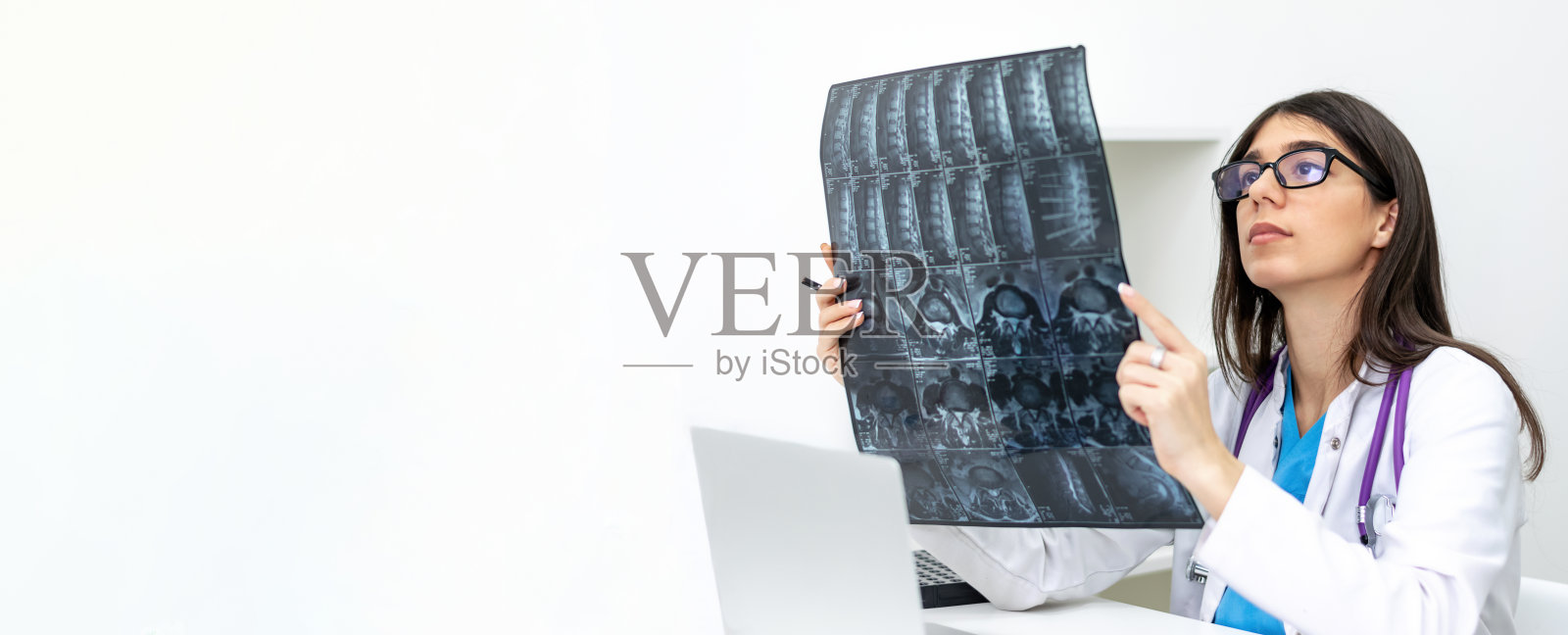 一位年轻的黑发女医生戴着眼镜，在诊所里检查核磁共振扫描。医学概念。照片摄影图片