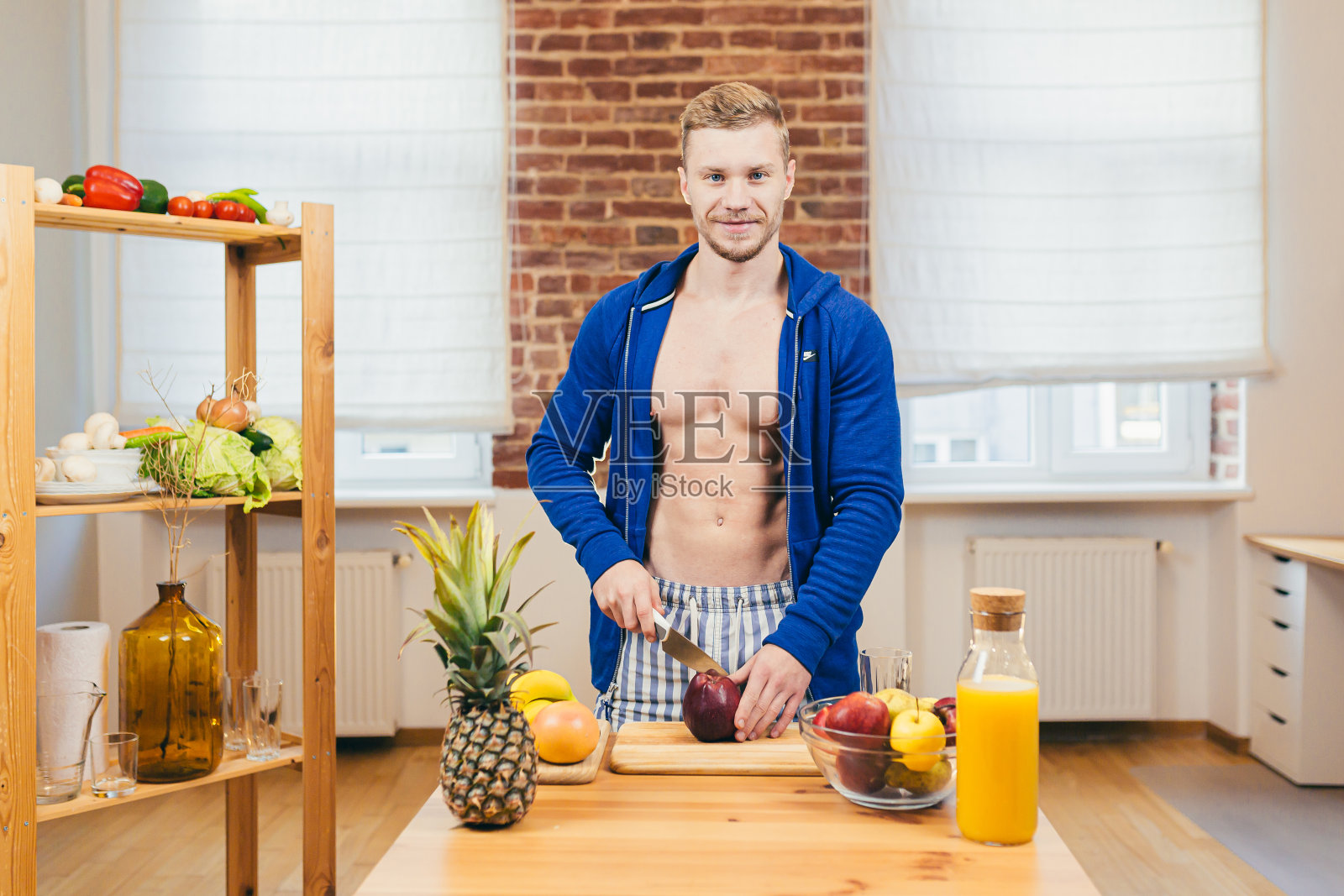 一个年轻英俊的健壮健壮的运动员站在家里的餐桌旁，切苹果，水果，健康的食物，微笑着看着镜头照片摄影图片
