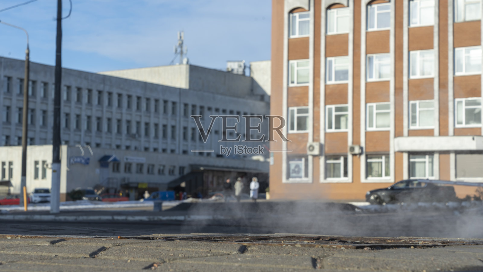 在寒冷的日子里，铺设的街道上的井盖，蒸汽从下面的下水道排出，进入城市街道。照片摄影图片