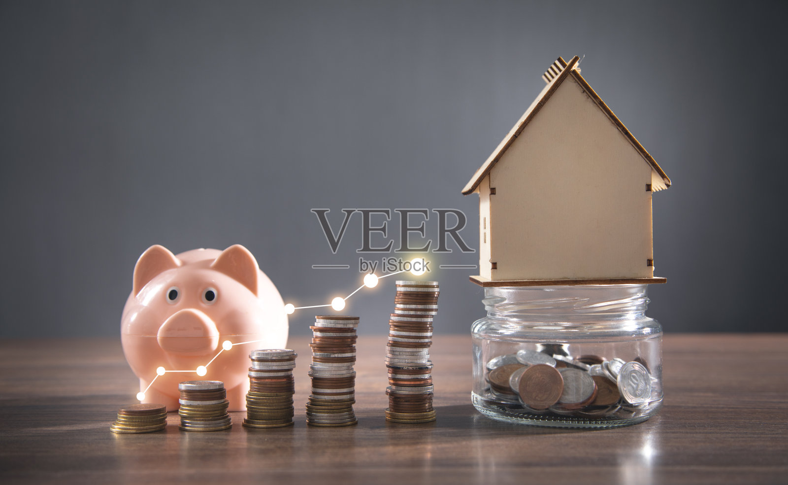 木桌上有房子模型、小猪存钱罐和硬币。照片摄影图片