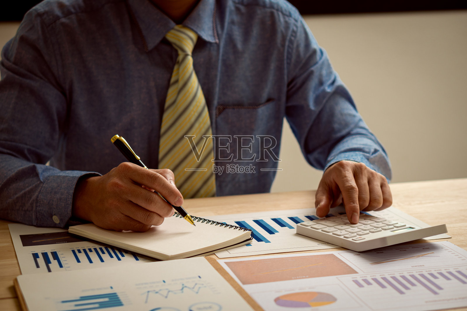 手按计算器，分析财务文件，同时在你的手指上拿着一支笔。年轻的亚洲商人收取税款，账单，信用卡付款，金融概念。照片摄影图片