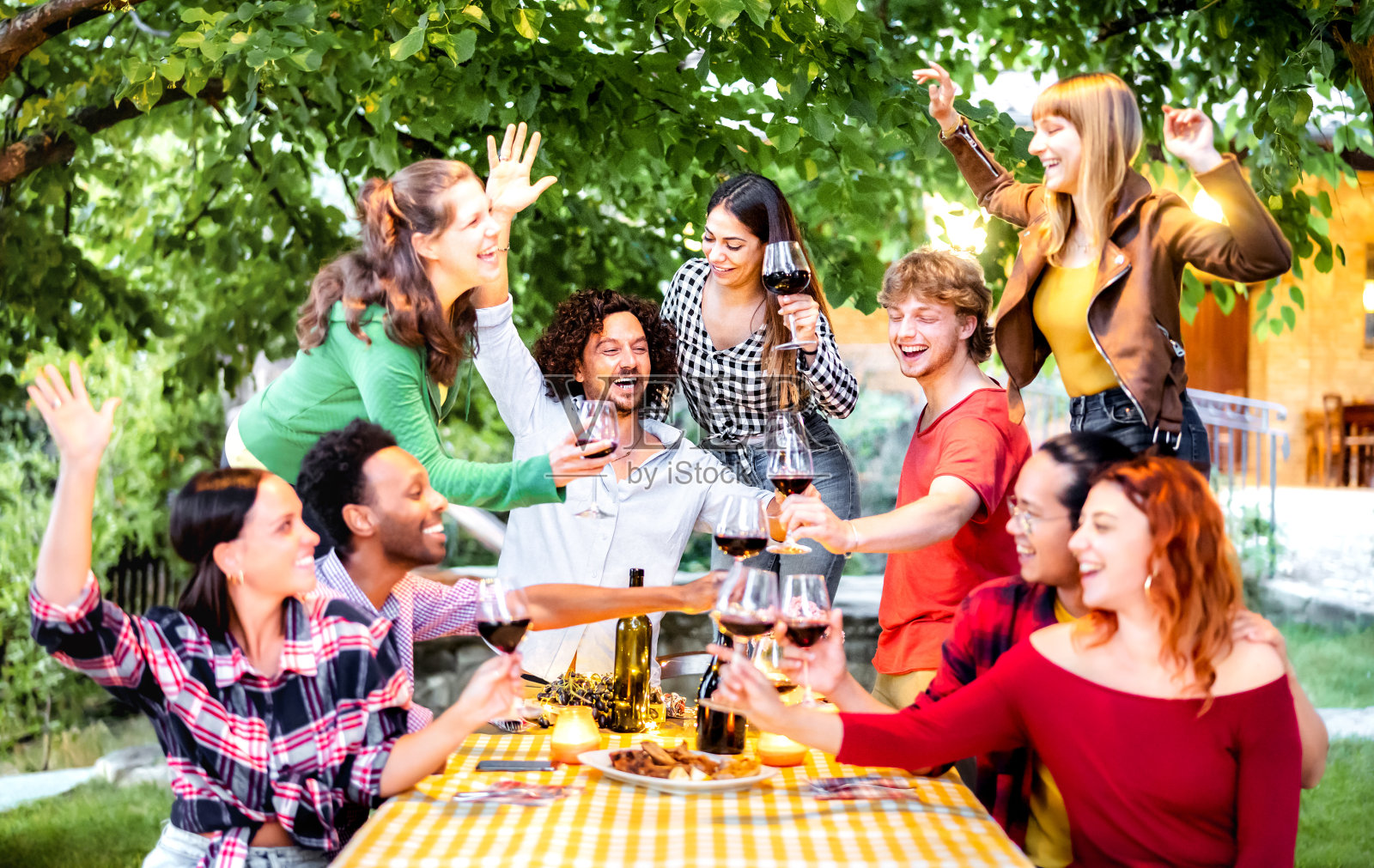 朋友们在露天派对上举杯畅饮-晚上人们在农舍酒庄一起吃饭喝酒-友谊的概念与浅深度的领域和集中在中间的家伙照片摄影图片