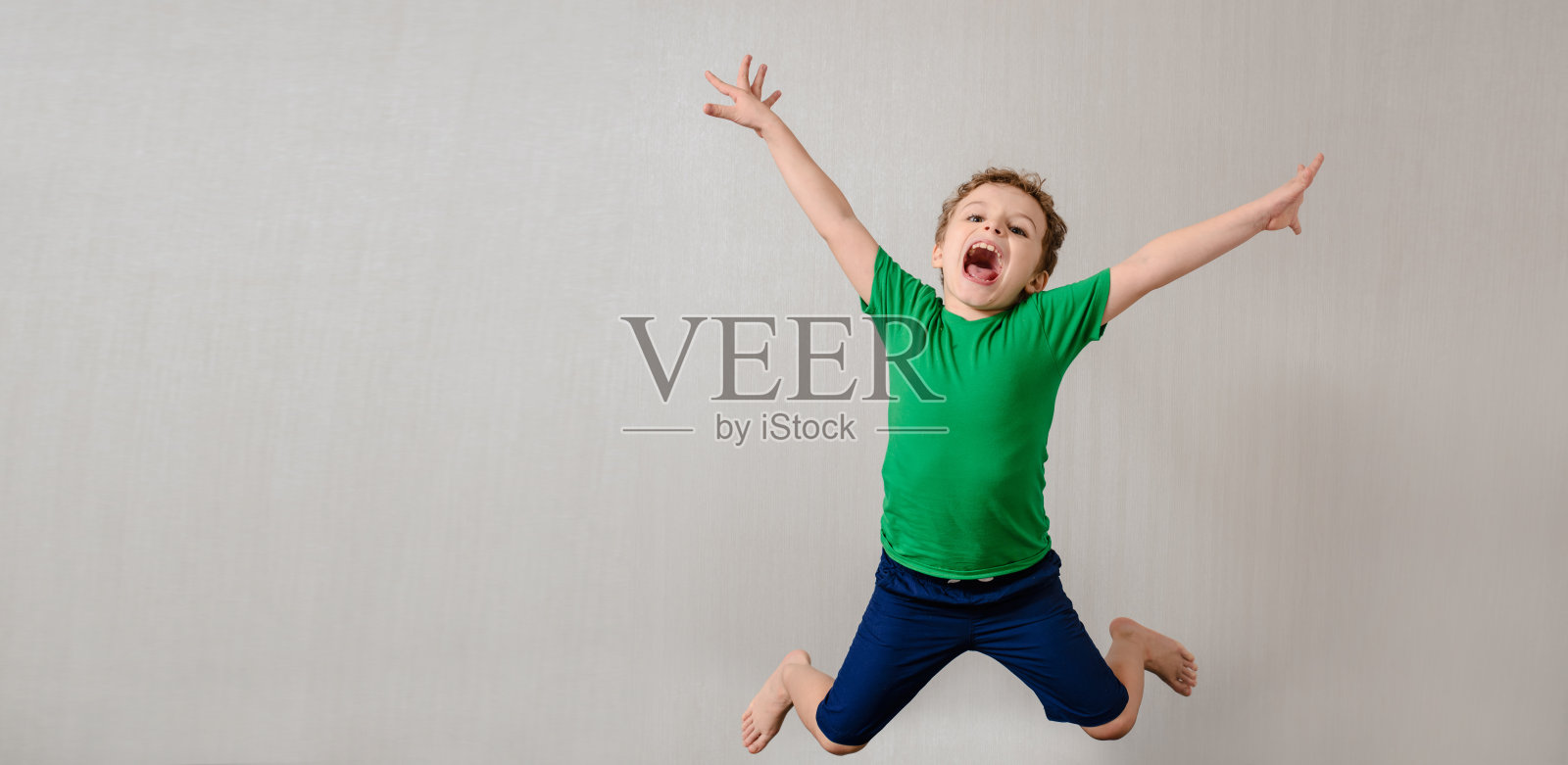 灰色背景上穿着绿色t恤的快乐小男孩在微笑，笑着，跳着照片摄影图片