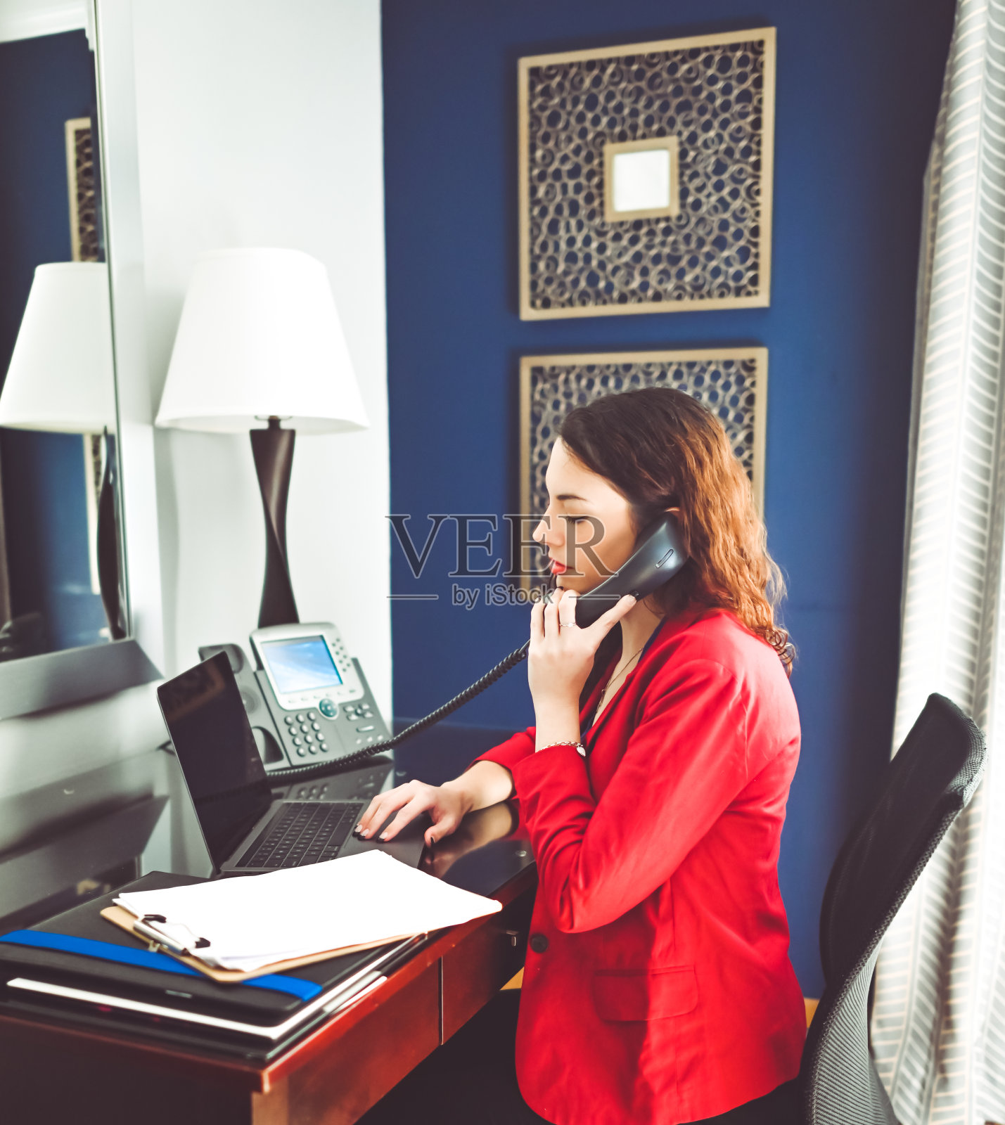 在有办公桌或办公室的酒店房间里工作的女性，专业人士用笔记本电脑打电话照片摄影图片