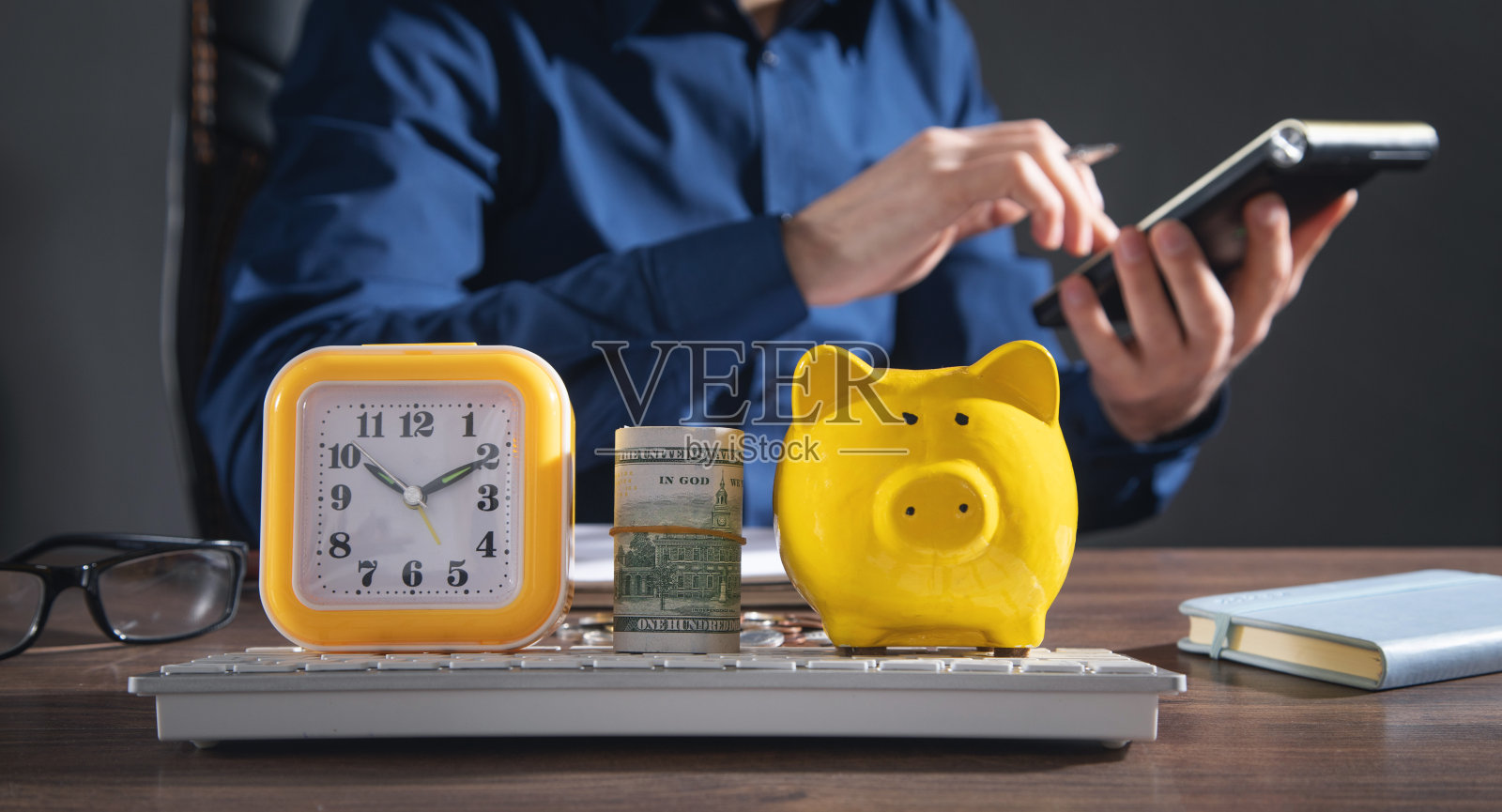 在办公室工作的商人，桌子上有一美元的钱，时钟和扑满。照片摄影图片