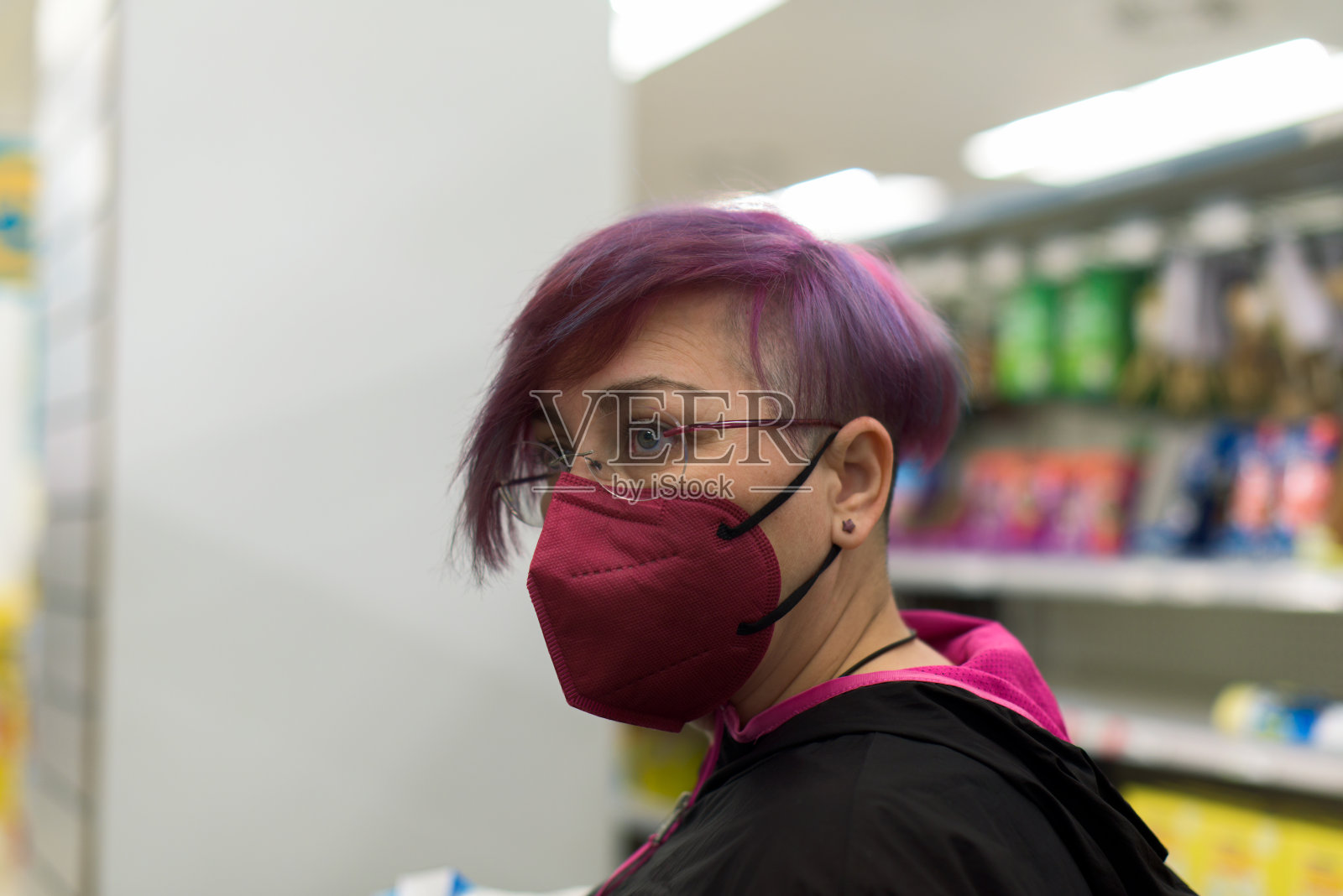一个留着紫色短发戴着防护口罩的女人在超市里。照片摄影图片