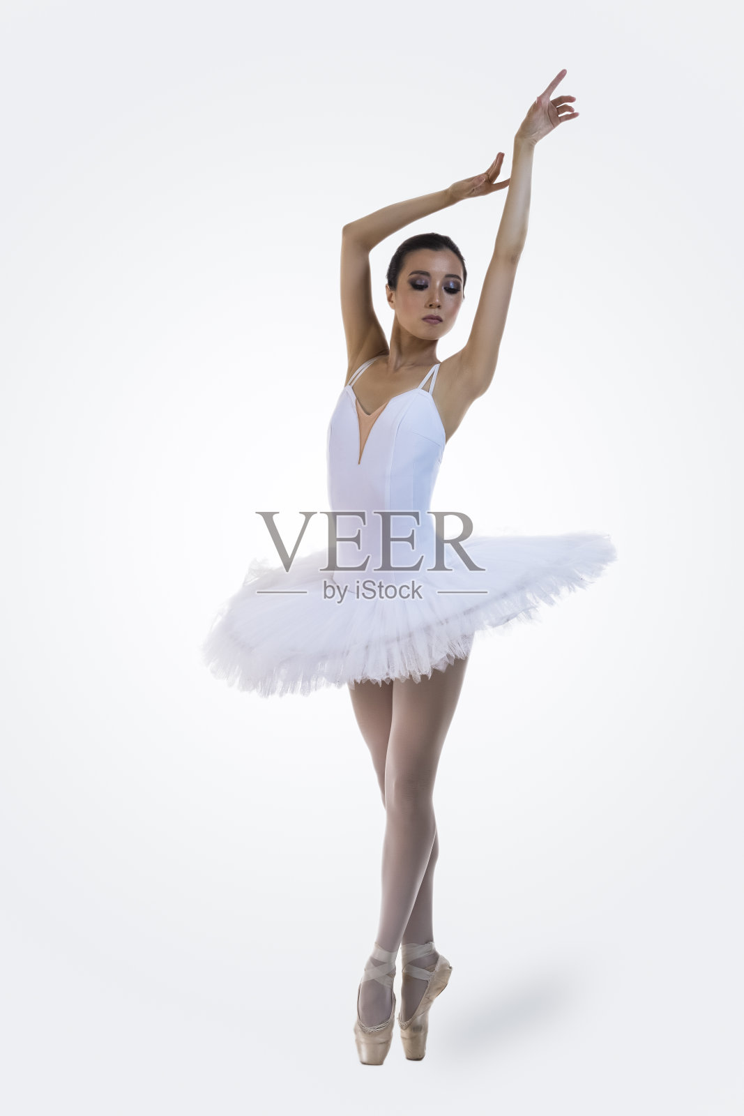 芭蕾舞蹈的概念。专业的日本女芭蕾舞演员在白色的背景下举起双手，穿着白色的芭蕾舞裙摆姿势。照片摄影图片