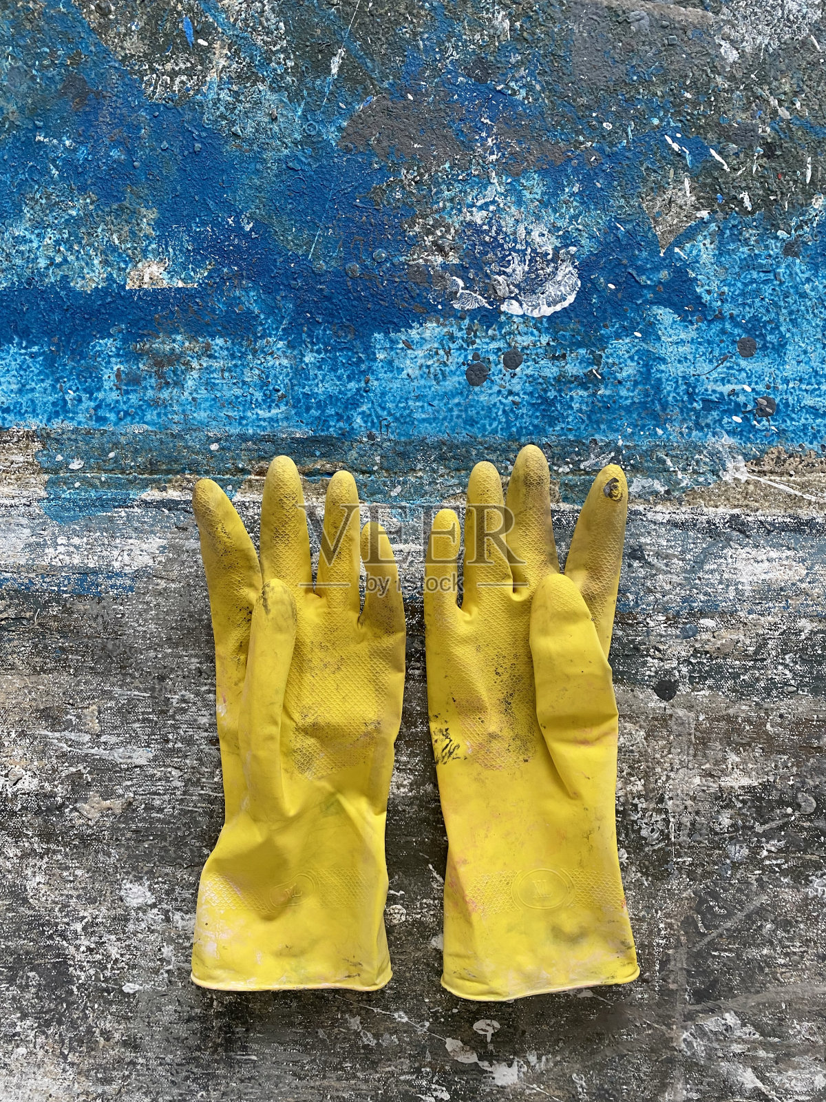 脏兮兮的黄色手套在涂成蓝色的旧混凝土上。艺术美学照片摄影图片