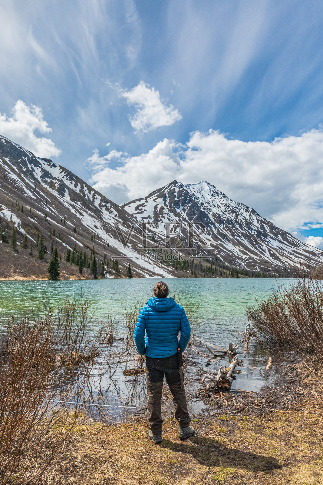 在加拿大北部，一名身穿蓝色夹克的男子站在一个巨大的湖边。照片摄影图片