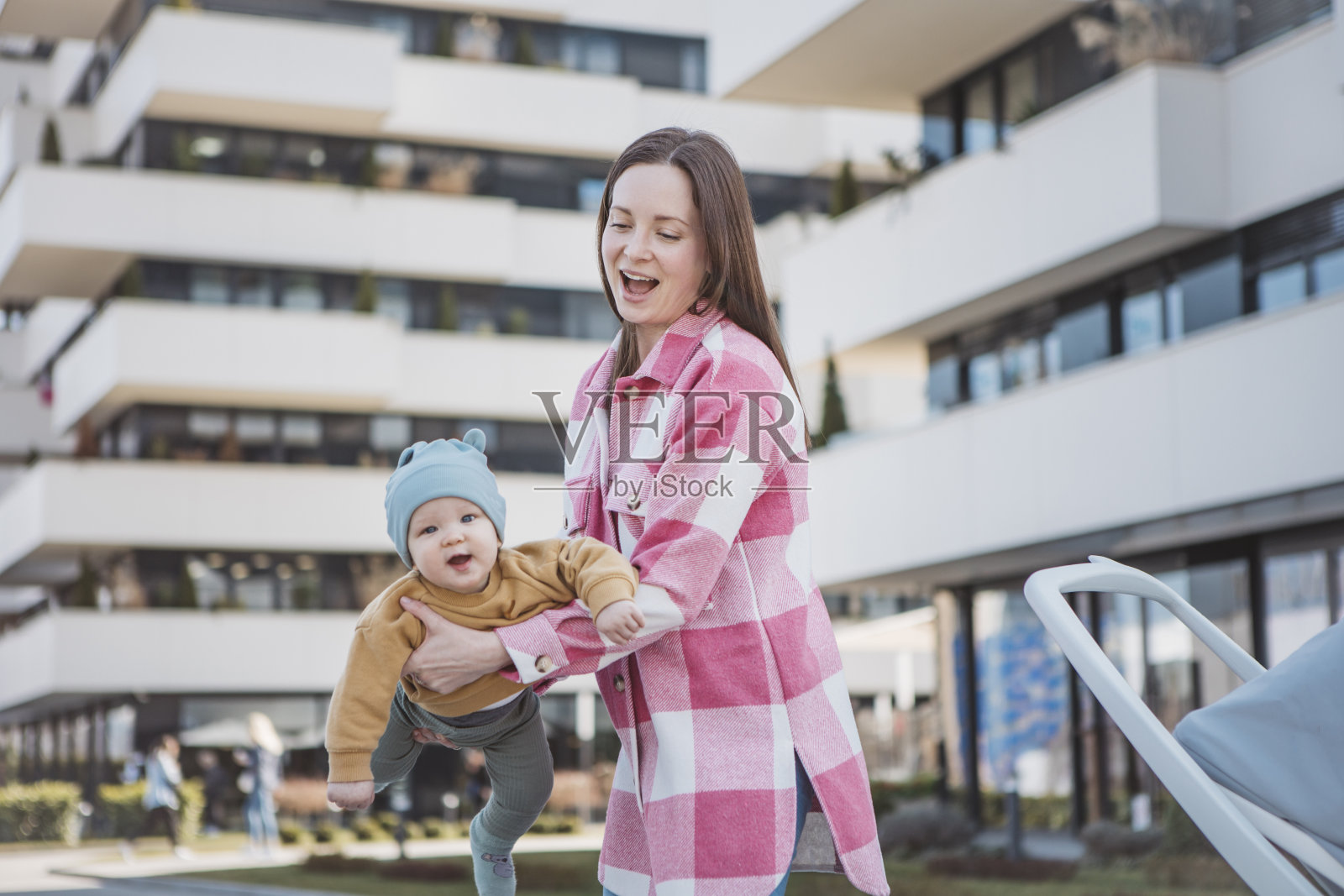 年轻的妈妈抱着婴儿，推着现代的婴儿车，漫步在城市中照片摄影图片