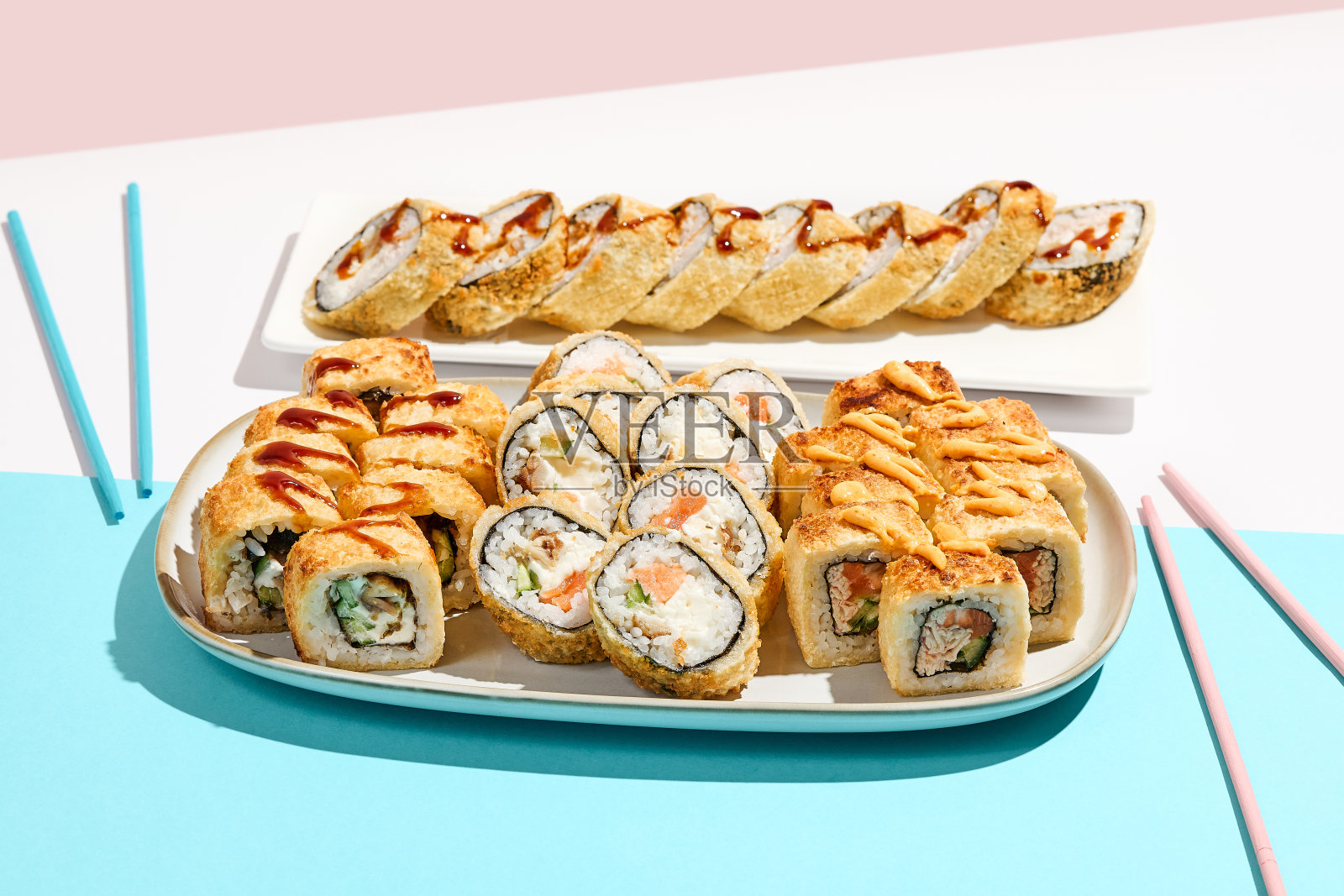 陶瓷餐具上设置的天妇罗寿司。热寿司配鳗鱼，鲑鱼，虾。现代日式菜单理念。用筷子夹在彩色背景上的寿司。天妇罗卷。照片摄影图片