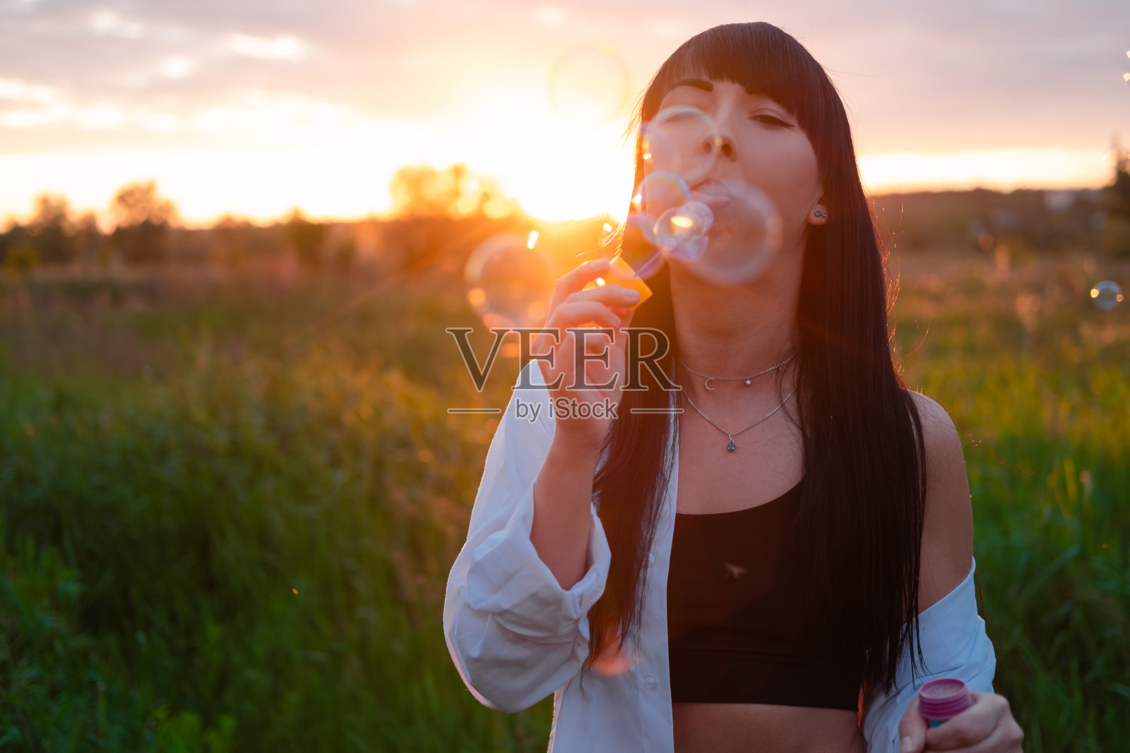 迷人的黑发女人在日落时在田野里吹肥皂泡照片摄影图片
