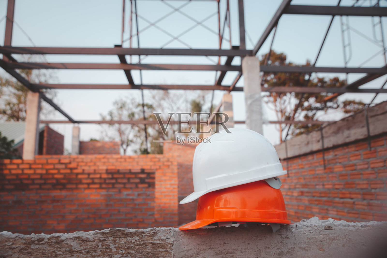 安全帽(安全帽)供工程师、安全员或建筑师使用，放置在水泥地面上，背景为砖。施工现场戴白色和橙色安全帽。照片摄影图片
