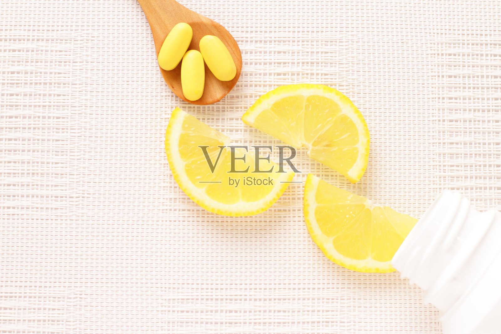 黄色的维他命放在勺子上，柠檬片做背景照片摄影图片