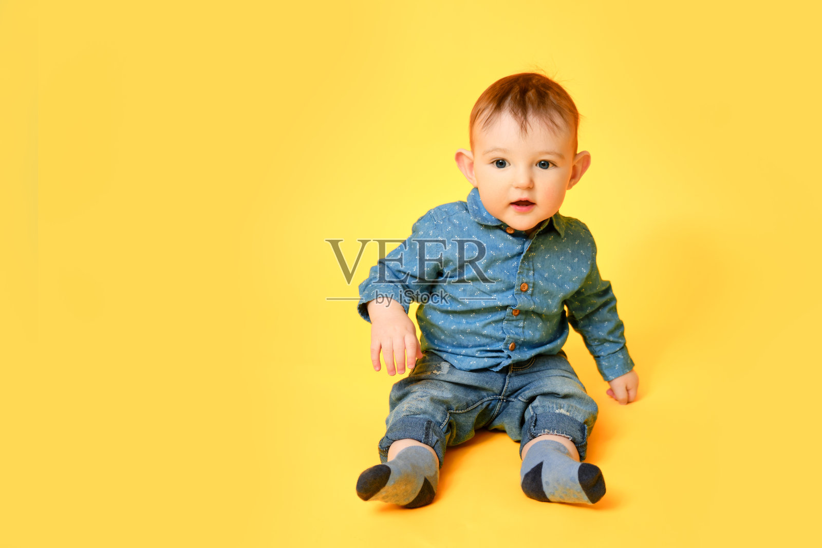 一个快乐的孩子在画室的黄色背景上穿着蓝色的衬衫和裤子。微笑的婴儿，穿着牛仔裤的小男孩照片摄影图片