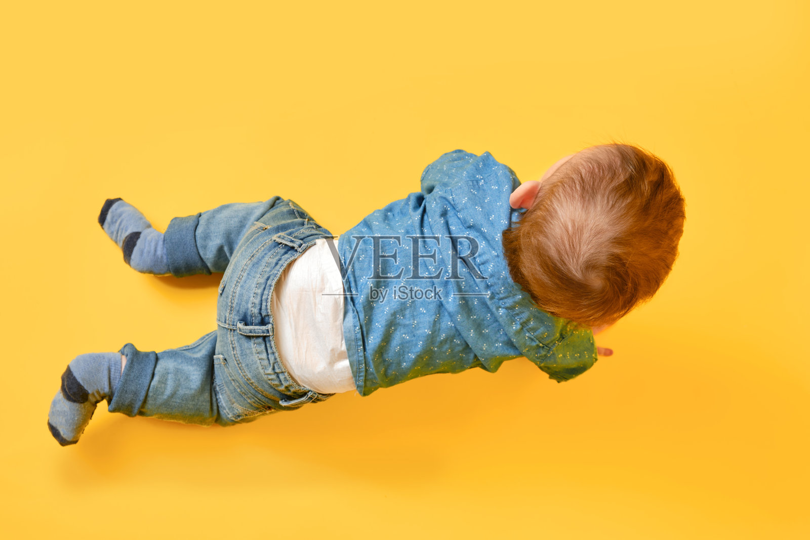 一个快乐的孩子在画室的黄色背景上穿着蓝色的衬衫和裤子。微笑的婴儿，穿着牛仔裤的小男孩照片摄影图片
