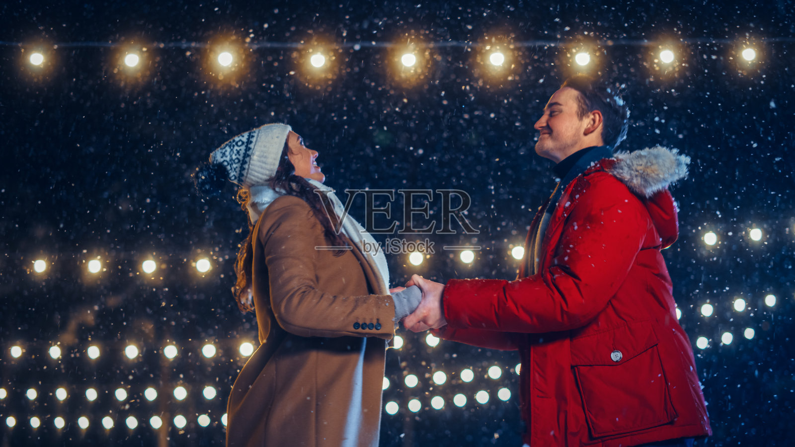 浪漫的冬雪之夜:滑冰情侣在溜冰场玩得很开心。双人滑冰男友和女友在爱，舞蹈，手牵手，拥抱，花样滑冰专业。中景镜头照片摄影图片