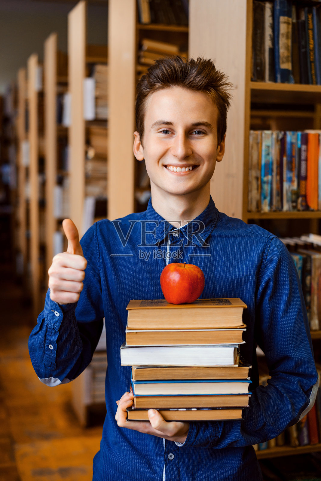 微笑的大学生，一堆要学习的书和一个苹果在上面照片摄影图片