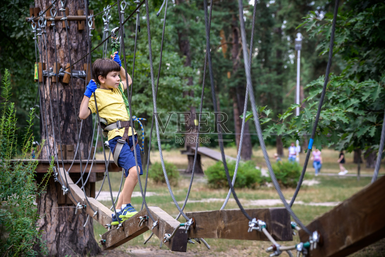 强壮兴奋的小男孩在户外玩绳公园。在温暖的阳光下穿着休闲服和运动鞋的白种人小孩。积极的休闲时间与孩子的概念照片摄影图片