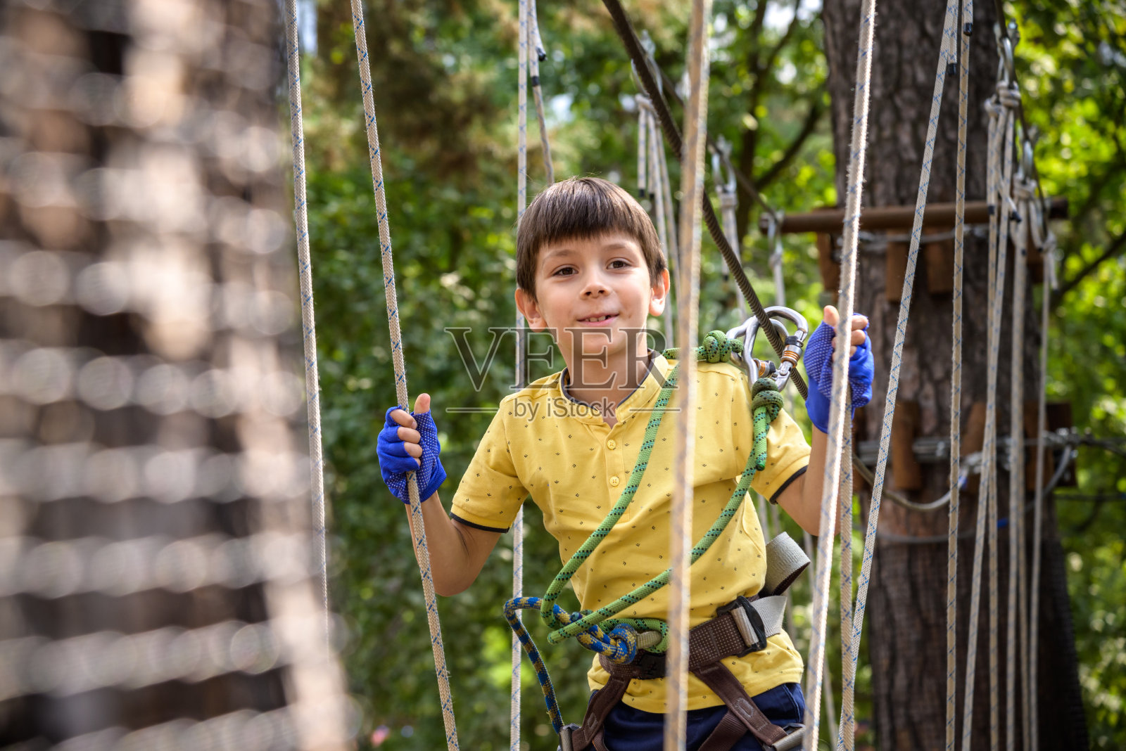 强壮兴奋的小男孩在户外玩绳公园。在温暖的阳光下穿着休闲服和运动鞋的白种人小孩。积极的休闲时间与孩子的概念照片摄影图片