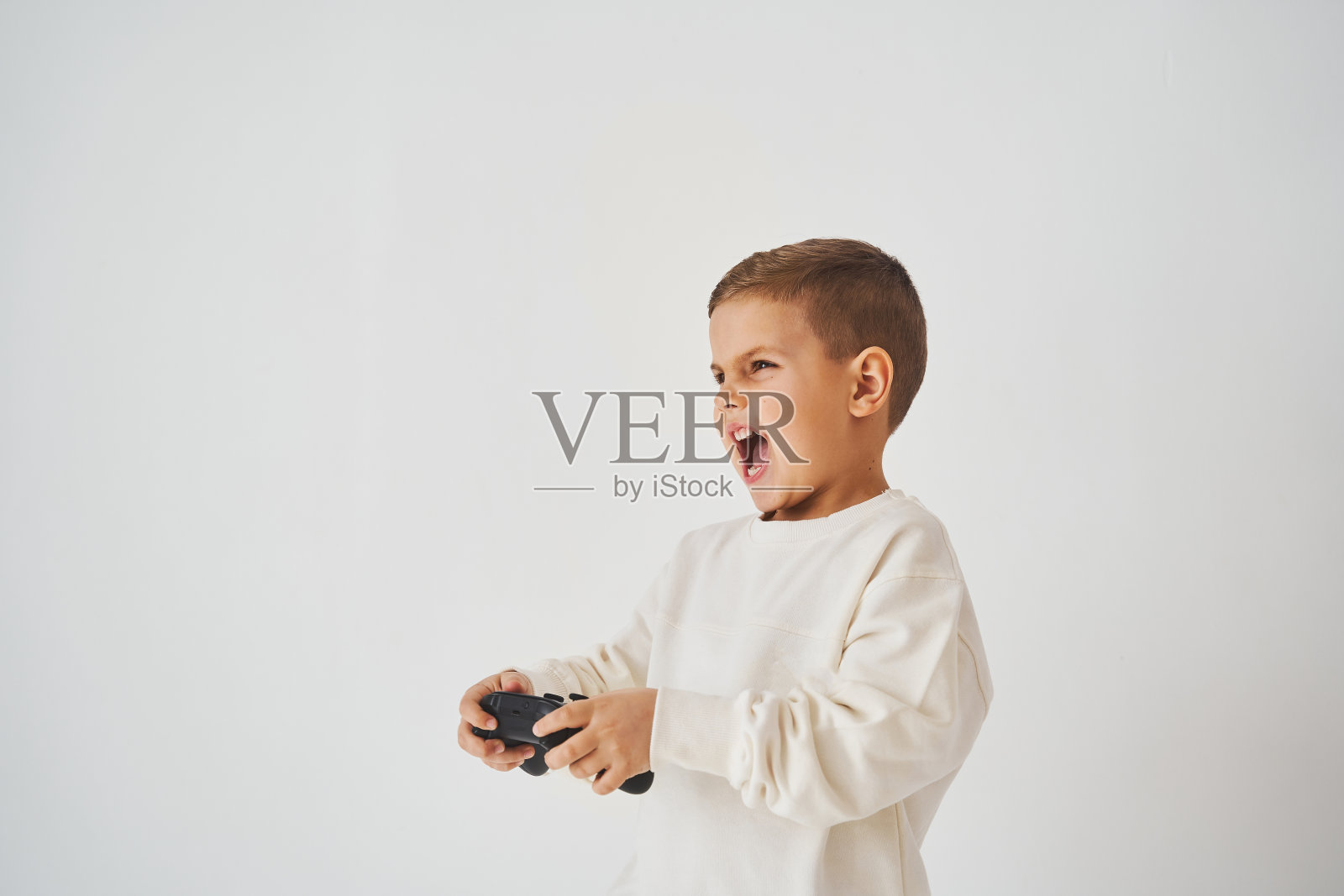 感情用事的孩子，游戏手柄在白色背景上。男孩在玩游戏。照片摄影图片