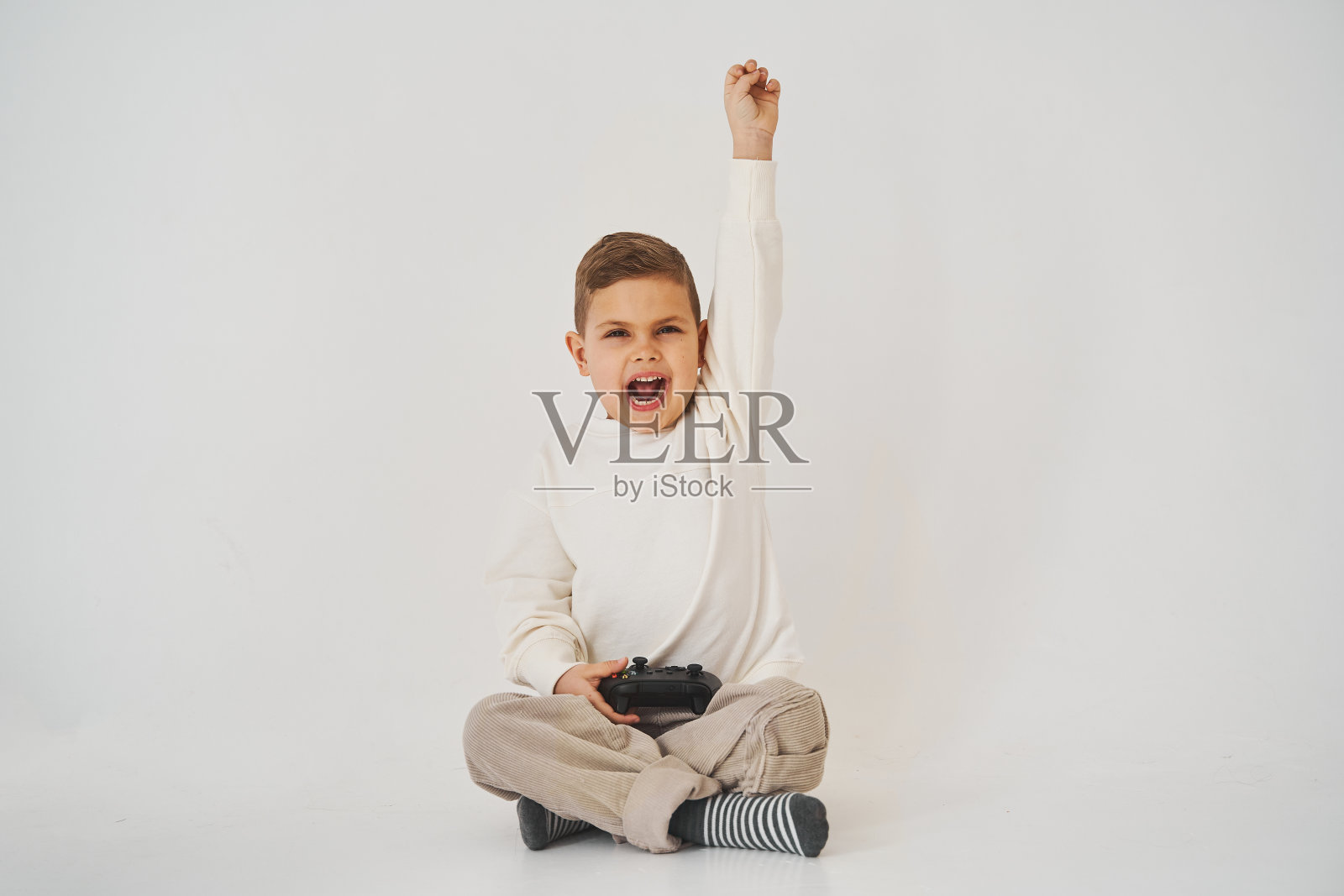 情绪激动的孩子拿着游戏手柄，因为他赢了游戏而欢呼、呼喊、举起双手。照片摄影图片