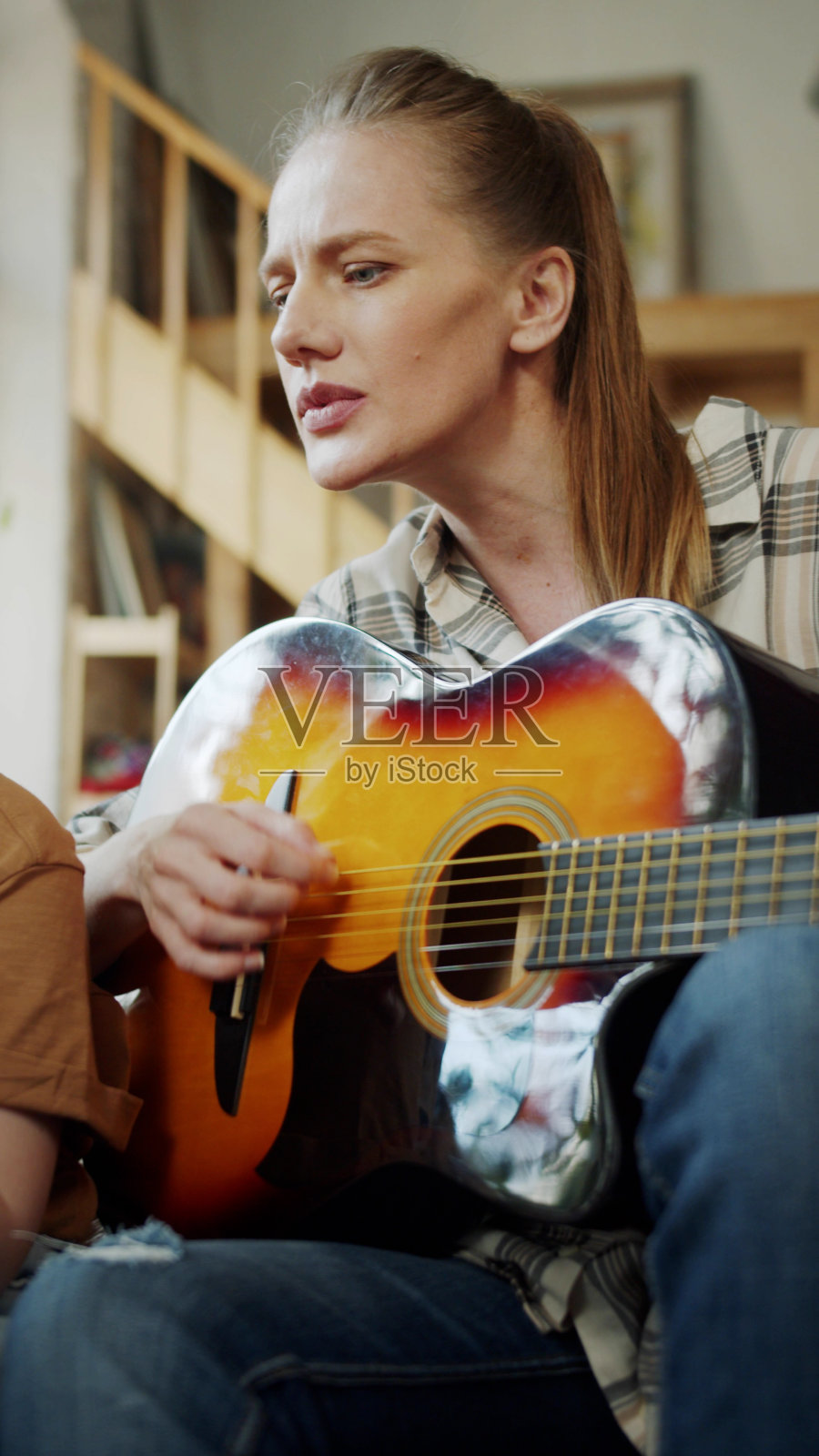 这个孩子帮他妈妈弹吉他。女孩拿着电话，母亲在看笔记照片摄影图片