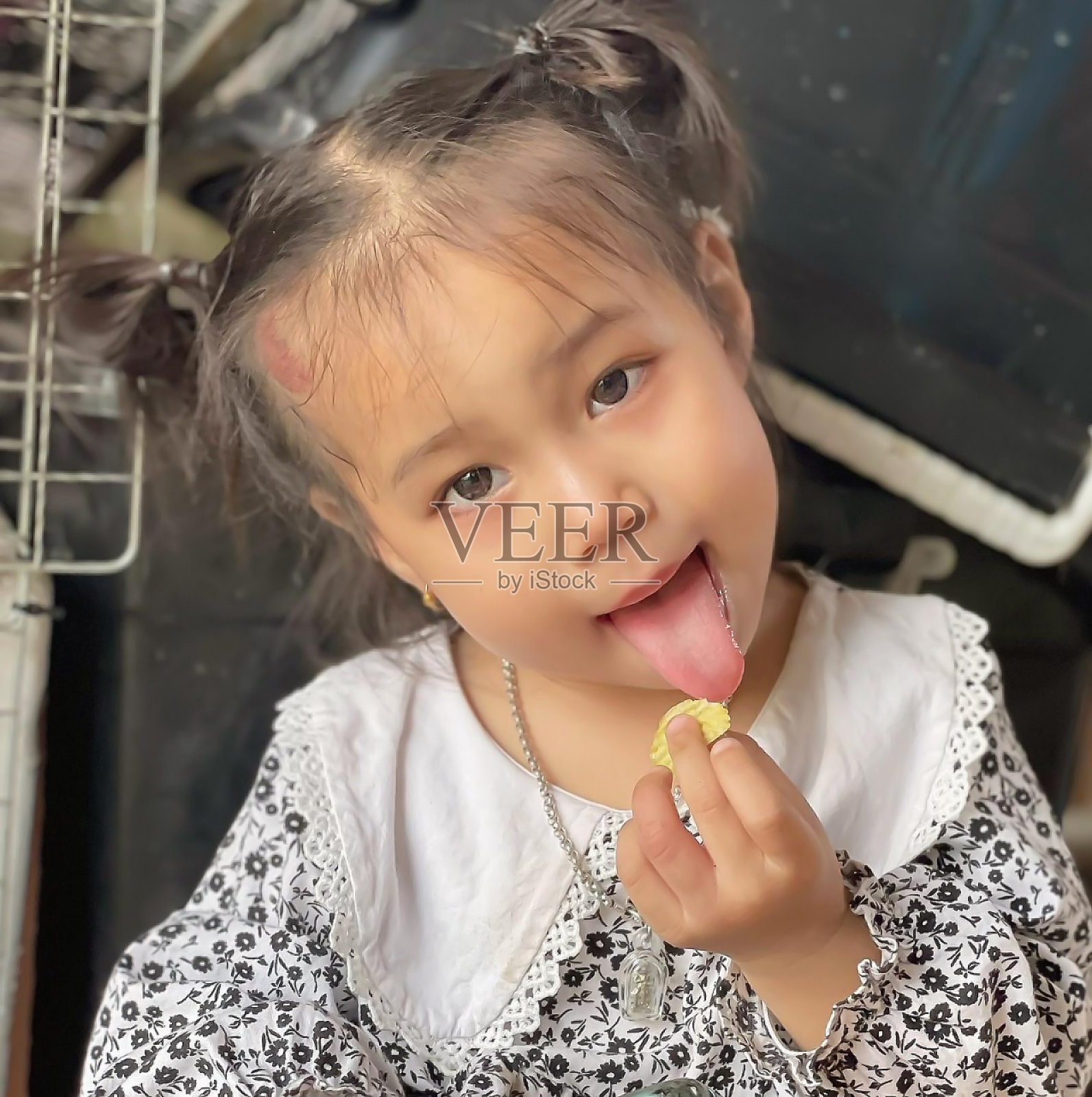 可爱的小女孩吃着零食，看着镜头，脸上露出了滑稽的表情，还伸出了舌头。快乐可爱的女孩肖像在家里。小孩子做了一个古怪的脸，看起来像母亲或某个人。照片摄影图片