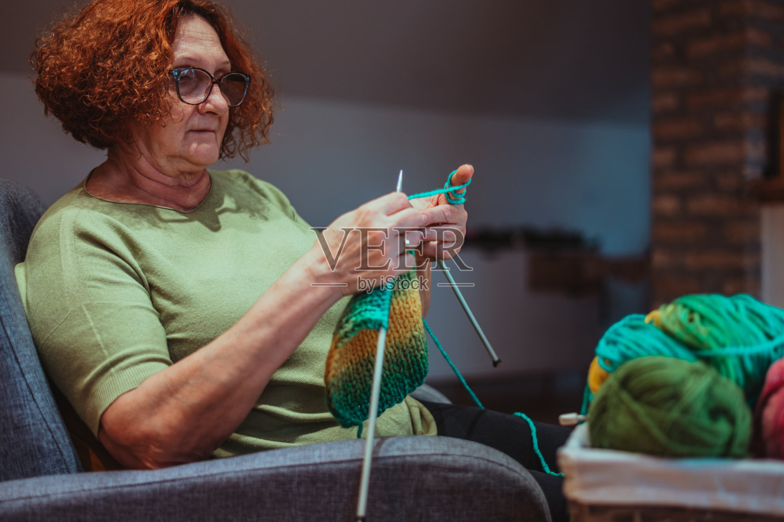 成熟的女人拿着编织针在家编织。照片摄影图片