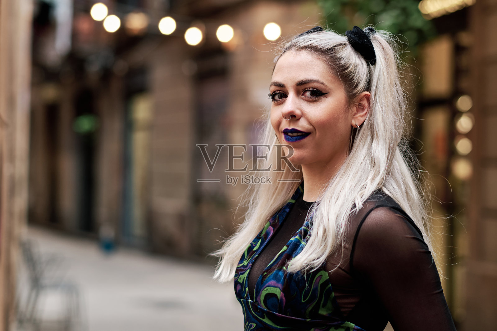 年轻的另类女子站在街上看着相机。照片摄影图片