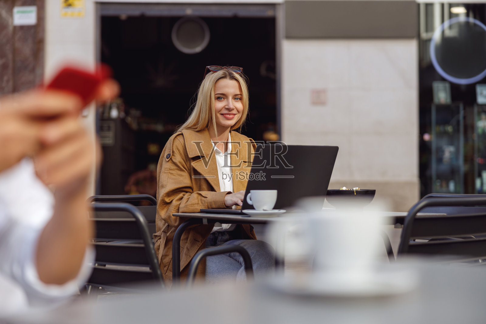 微笑的女性看着相机，而坐在桌子的街头咖啡馆照片摄影图片