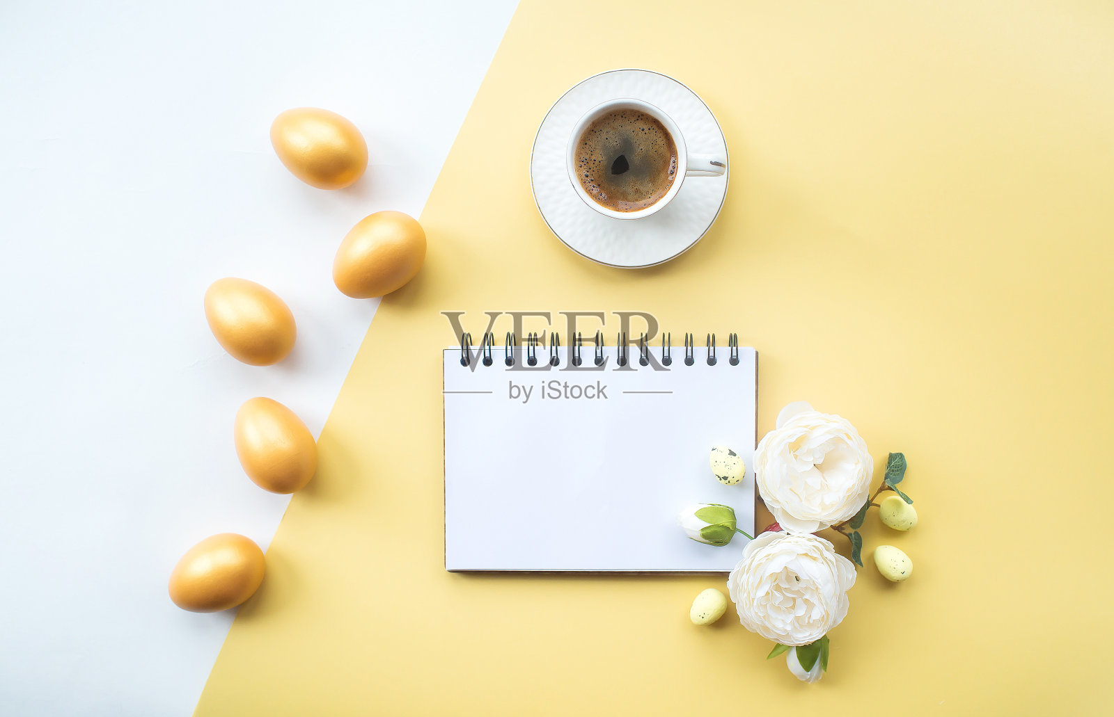 金色的复活节彩蛋，咖啡杯，精致的花和笔记本与地方的文本在黄色的背景上。时髦的公寓。最小的概念。照片摄影图片