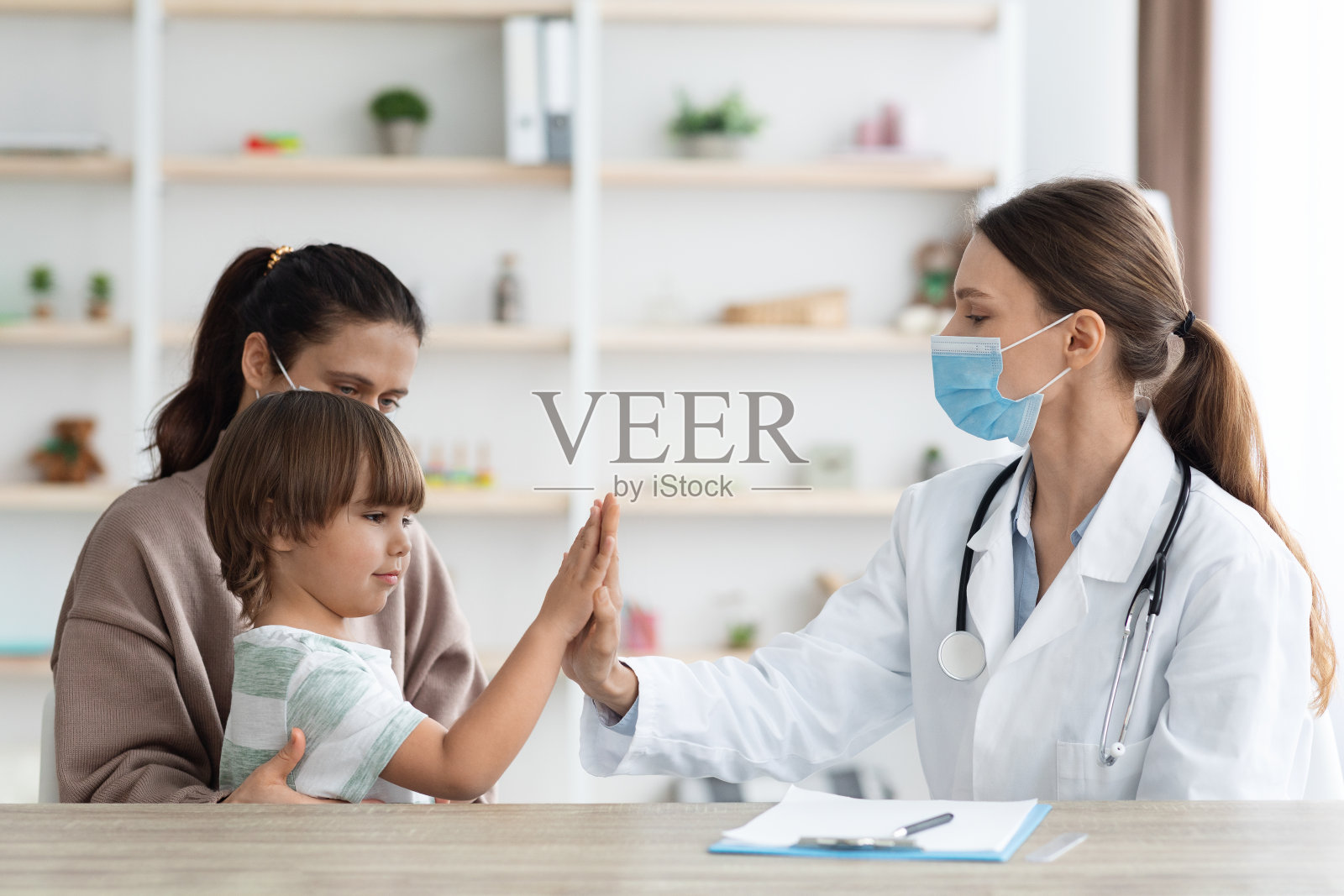 快乐的小男孩给职业女医生击掌，与母亲坐在办公室，空照片摄影图片