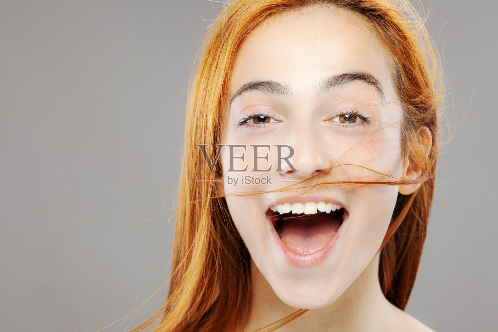 快乐的红发女孩摆姿势。工作室肖像在灰色的背景照片摄影图片