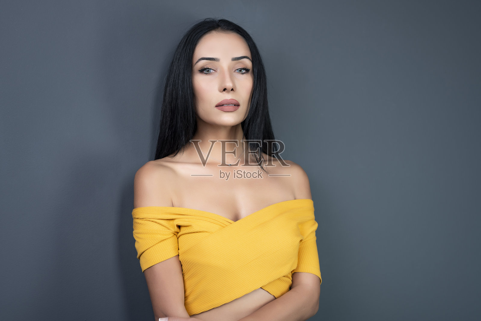 一名迷人的年轻女子，穿着黑色的裙子和闪亮的布料，黄色的衬衫，黑色的长发和黑色的长靴，在一个灰色的工作室里拍照。照片摄影图片