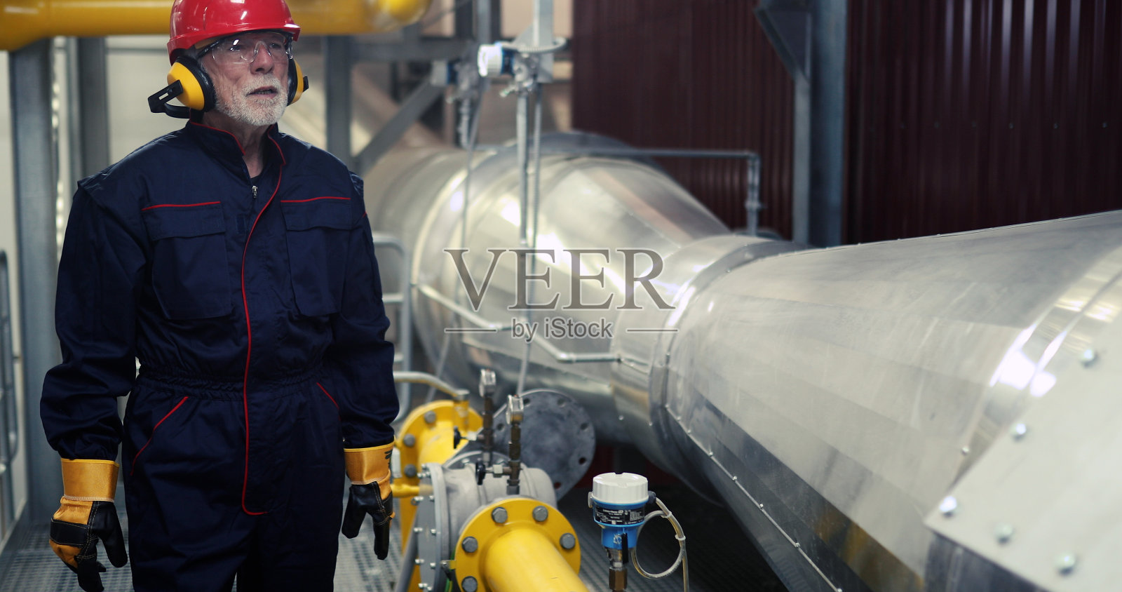 一名穿着制服的工人检查供热厂的管道是否正常工作。照片摄影图片