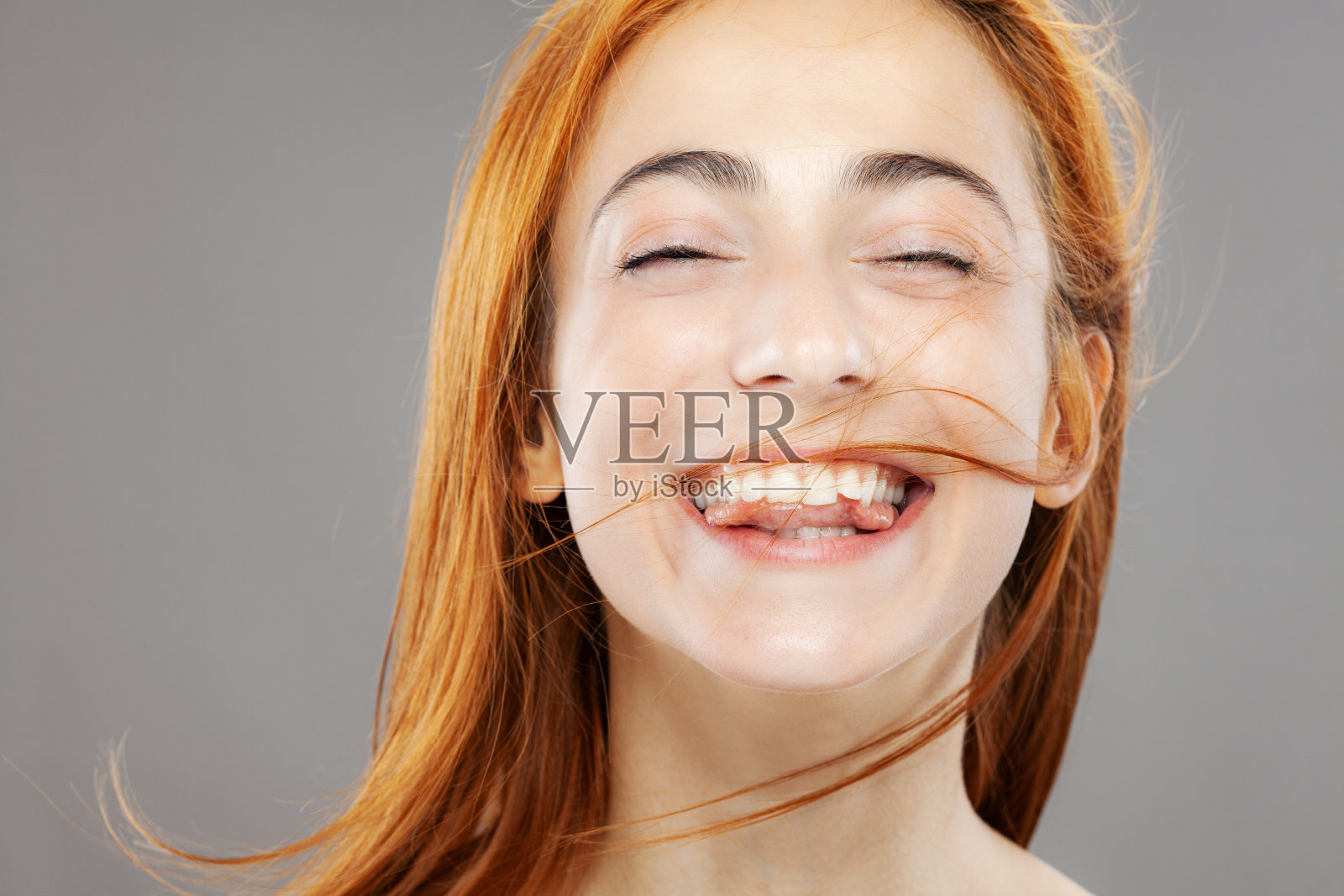 快乐的红发女孩摆姿势。工作室肖像在灰色的背景照片摄影图片