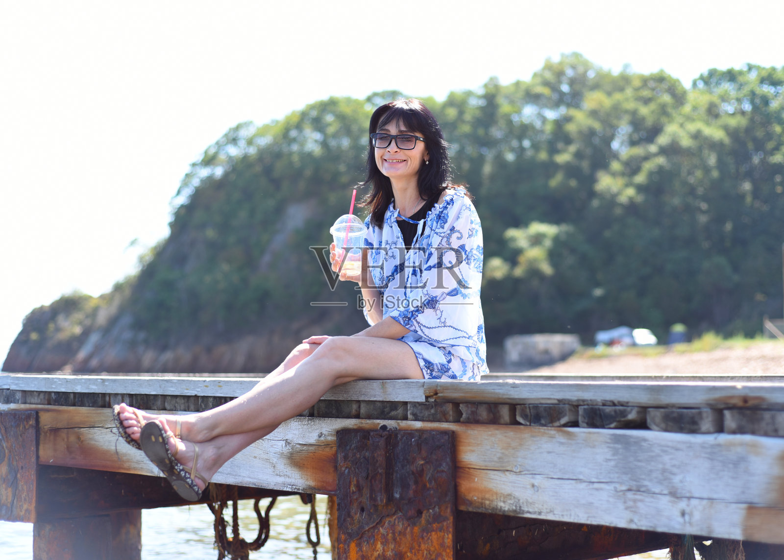 45岁的俄罗斯女人喝柠檬水，坐在码头上照片摄影图片