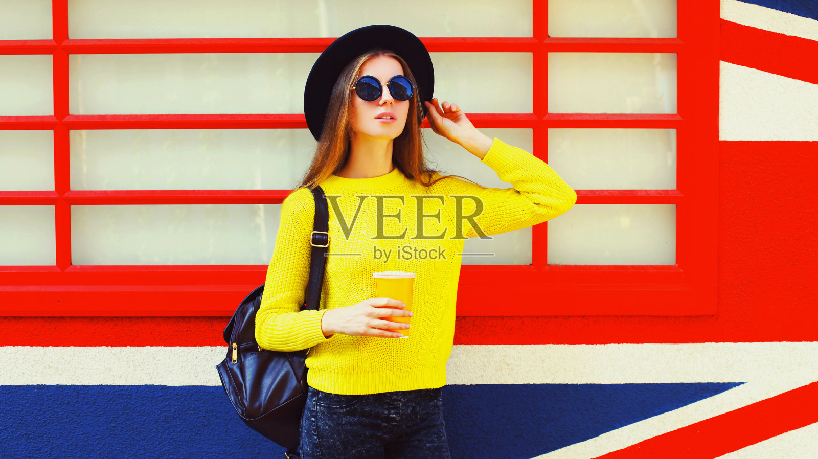 美丽的年轻女子的肖像与一杯果汁在英国国旗墙的背景照片摄影图片