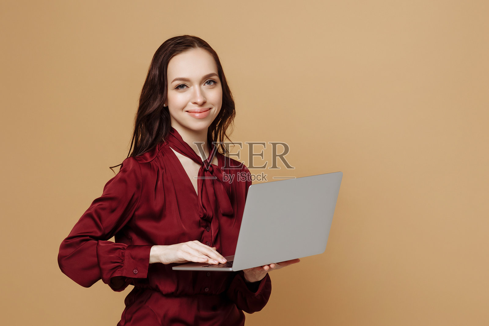 愉快的年轻女子站在孤立的米色背景和使用笔记本电脑。照片摄影图片