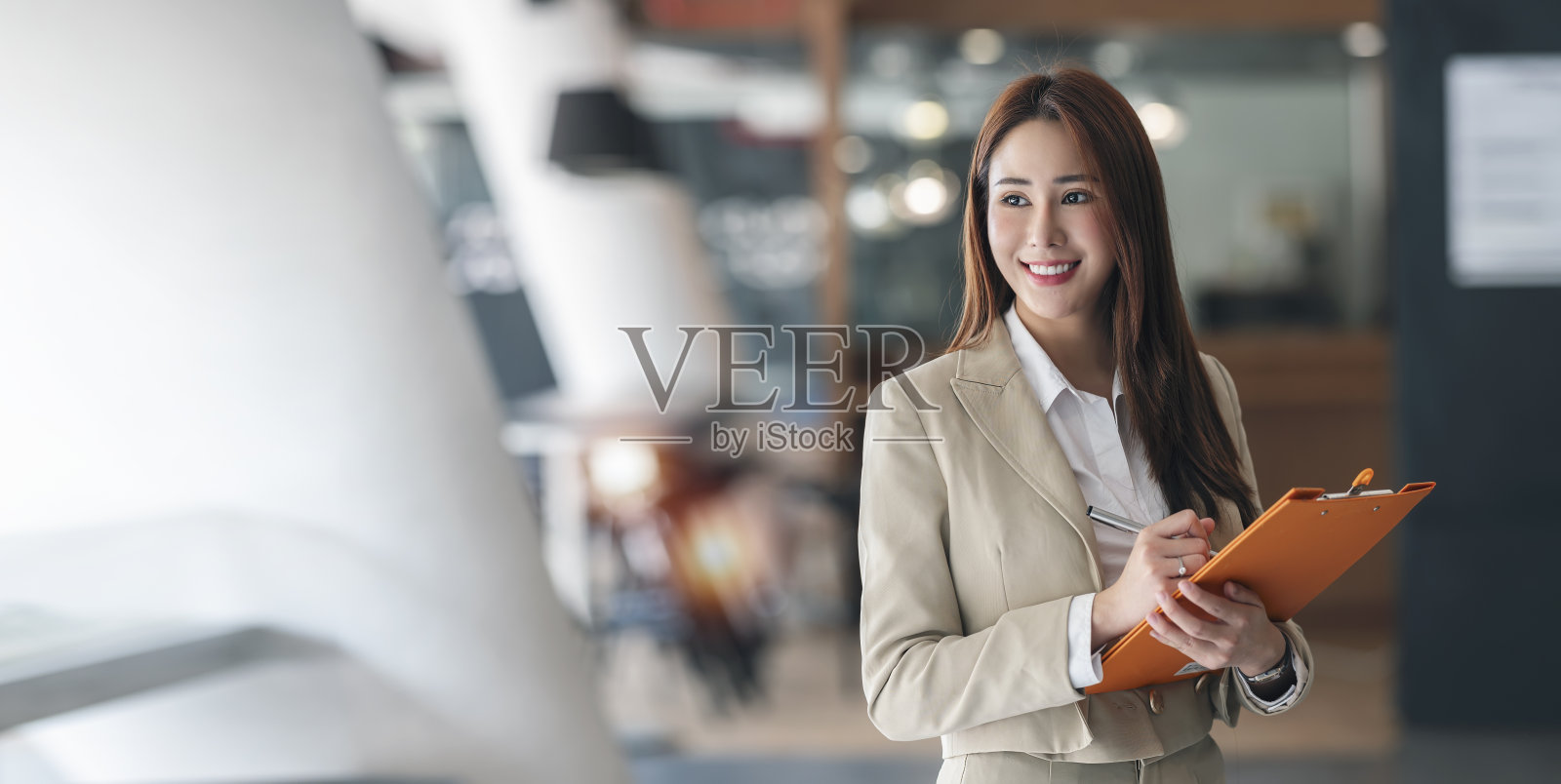 美丽的女商人的肖像，拿着文件夹，微笑着看着外面，而站在办公室里。照片摄影图片