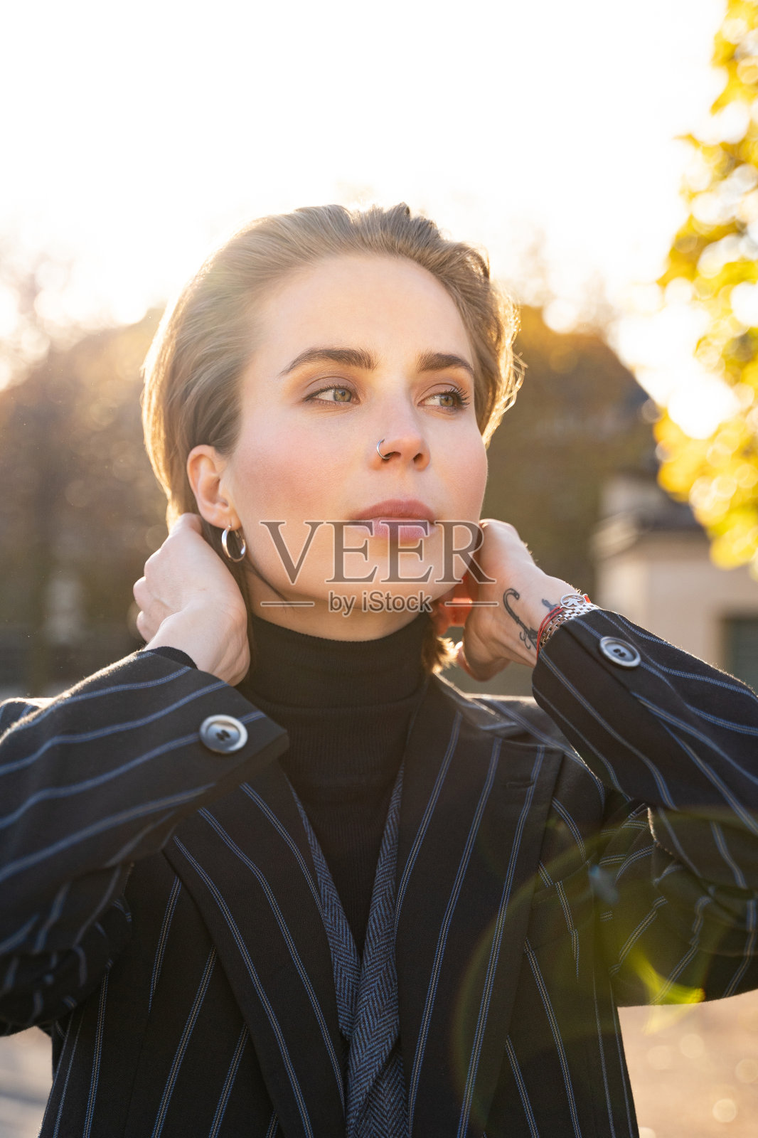 年轻的金发女人穿着条纹夹克和毛衣在公园里拉直她的头发照片摄影图片