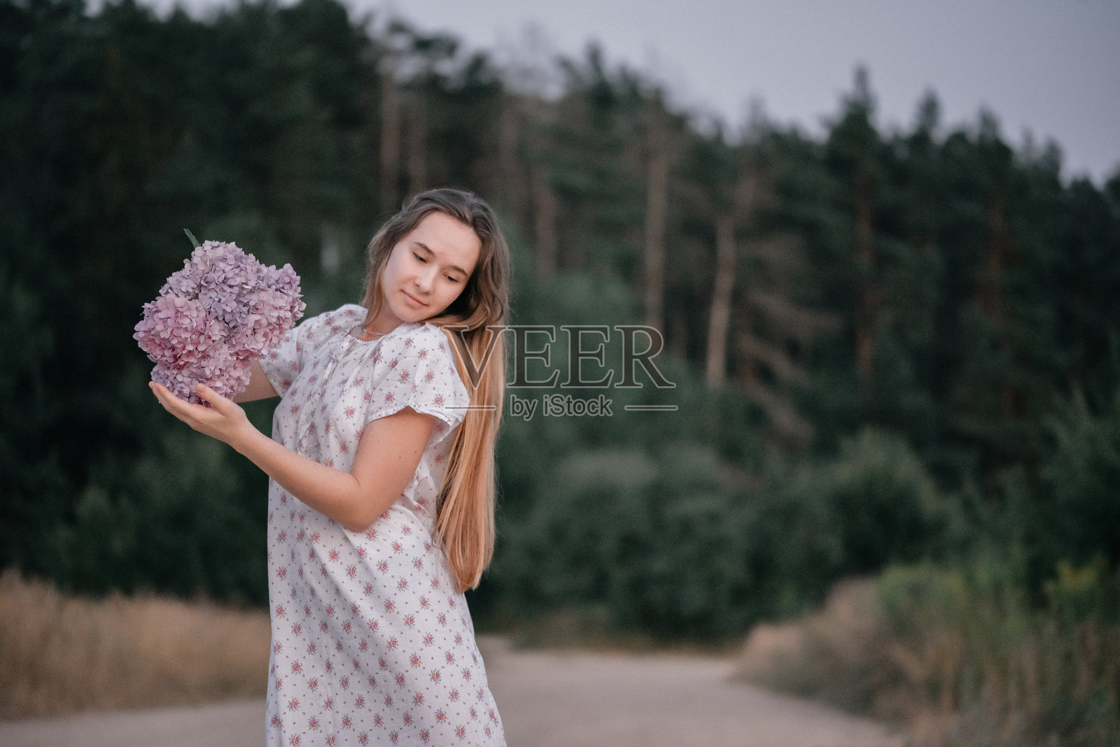 森林边的女孩手里捧着花。照片摄影图片