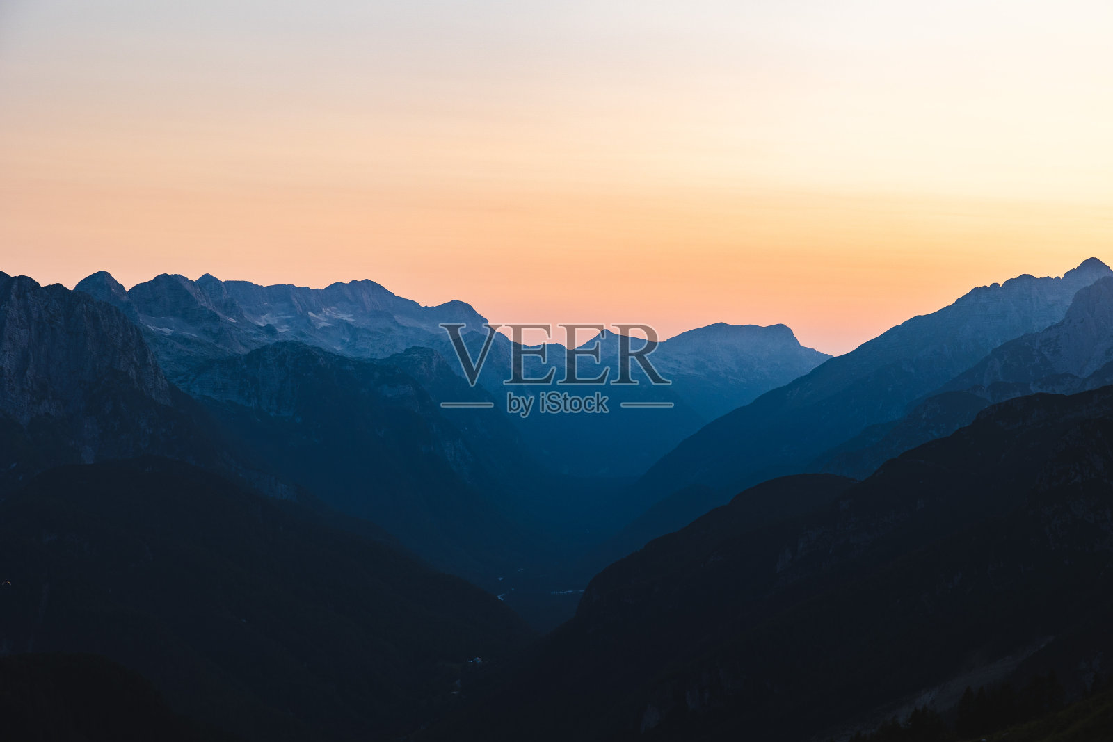 在晴朗的天气下，从黑色到蓝色的阴影和橙色日落的山脉景观的近距离视图照片摄影图片