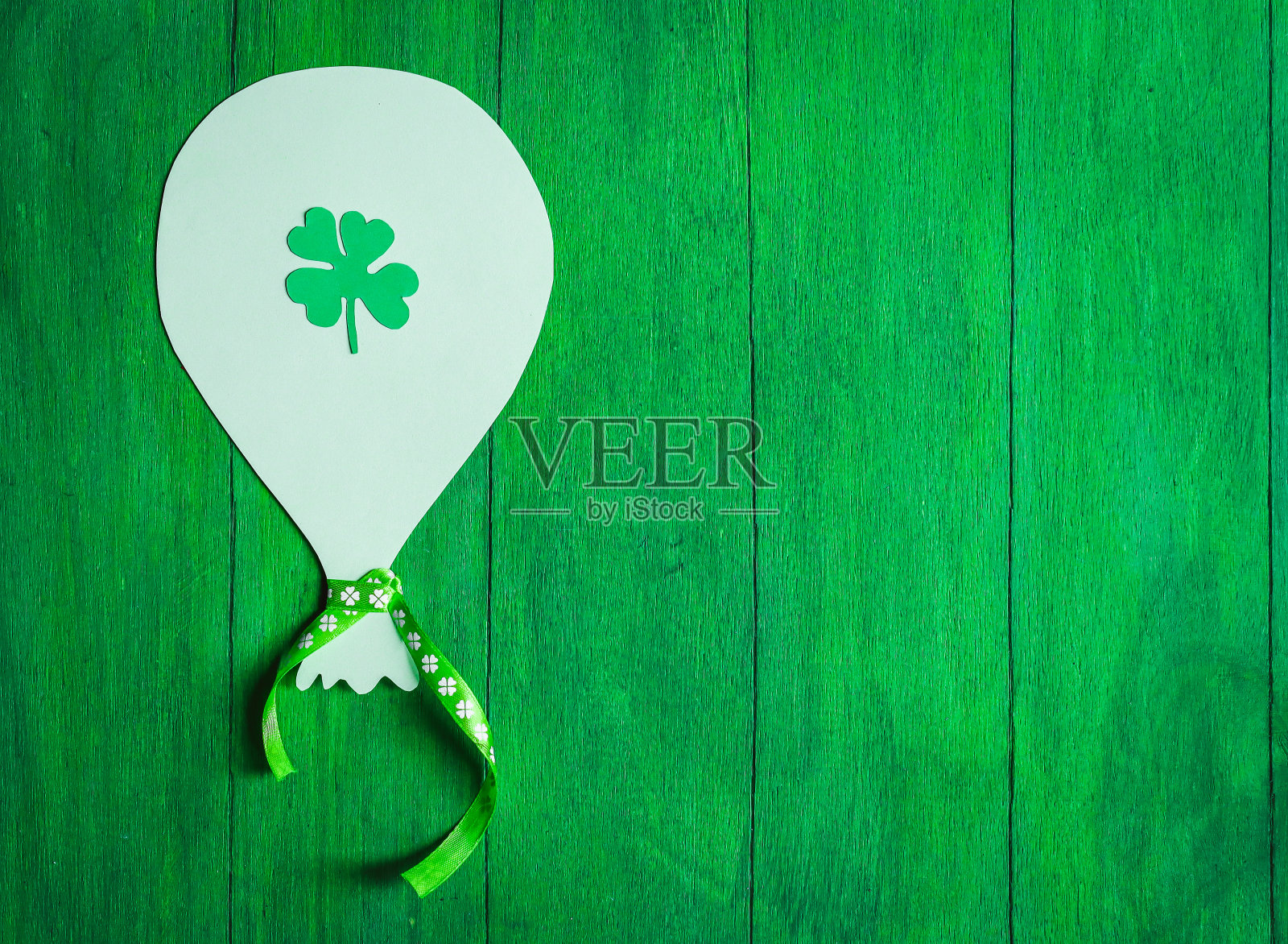 一个有丝带和三叶草叶子的手工剪纸球在绿色的木质背景上。照片摄影图片